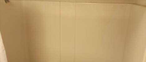 Baño con cortina de ducha, cabezal de ducha visible y pared con azulejos.