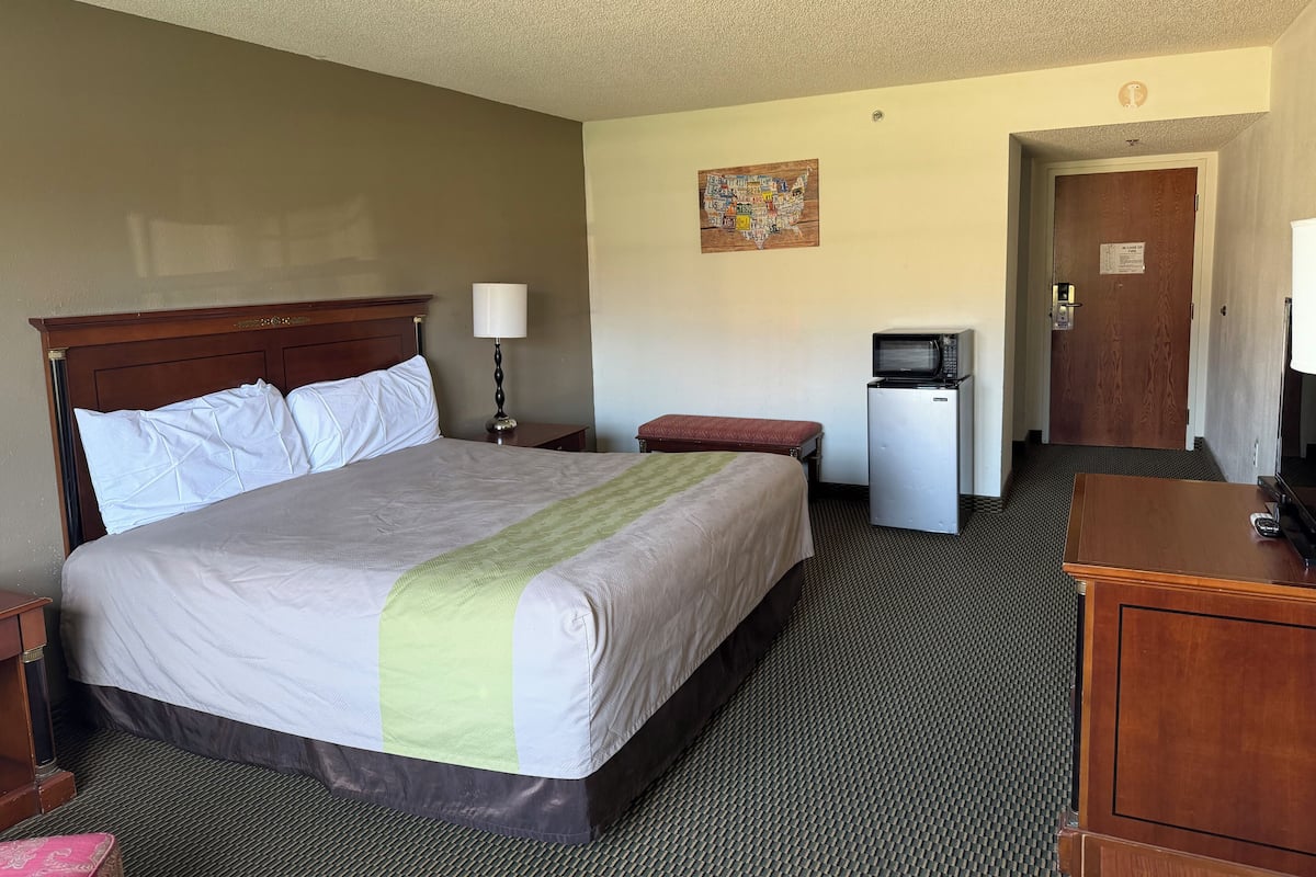 A hotel room with a bed, a desk, a lamp, a microwave, and a door.
