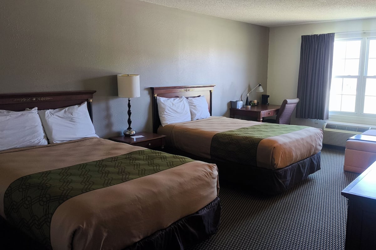 A hotel room with two beds, a desk, a chair, a lamp, and a window with curtains.