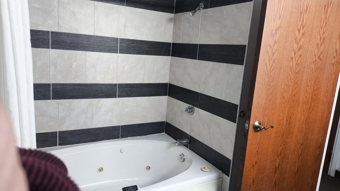A bathroom with a bathtub, black and white tiles, and a wooden door.