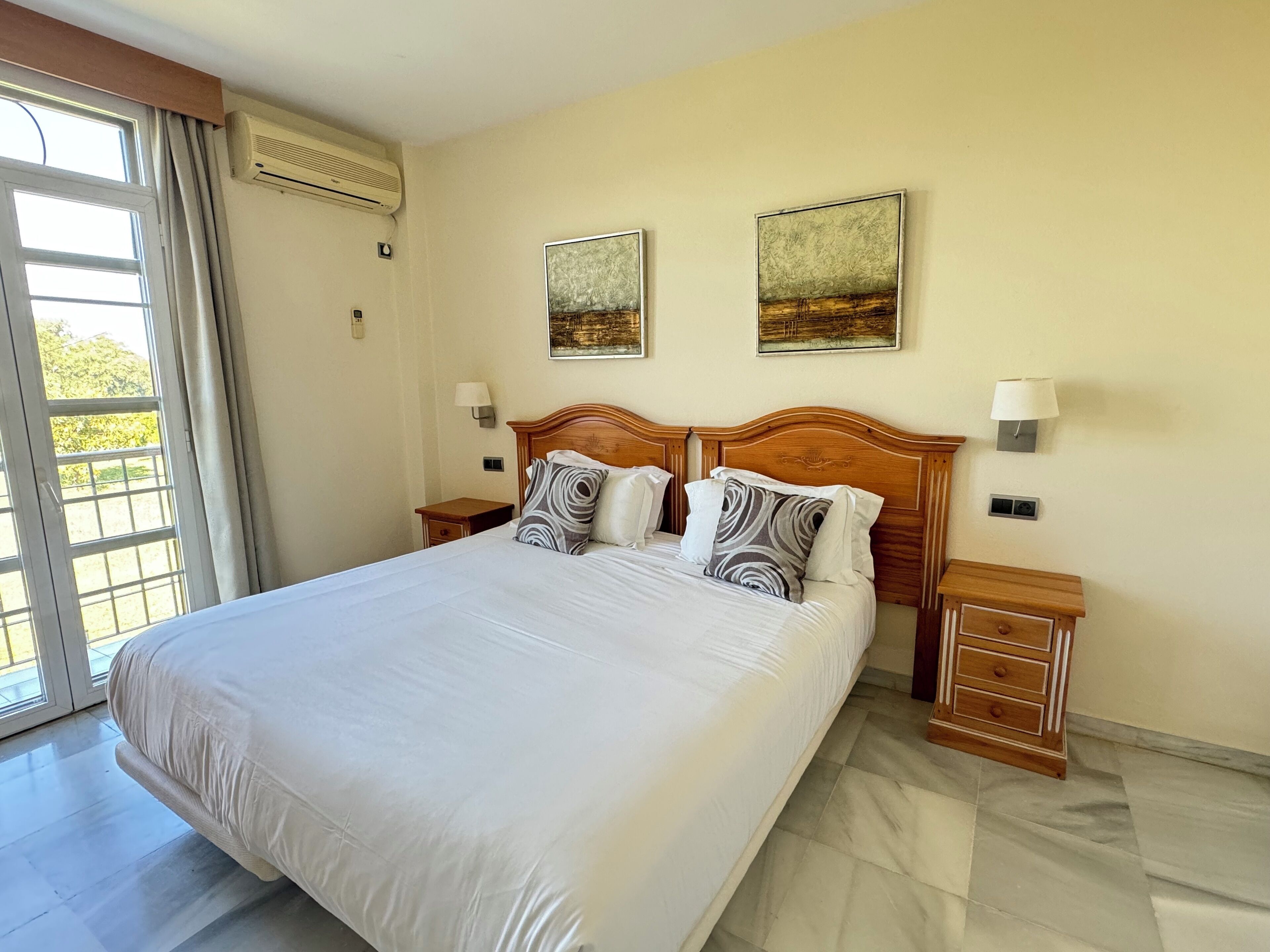A hotel room with a large bed, two bedside tables, a wooden headboard, and two wall-mounted lamps.