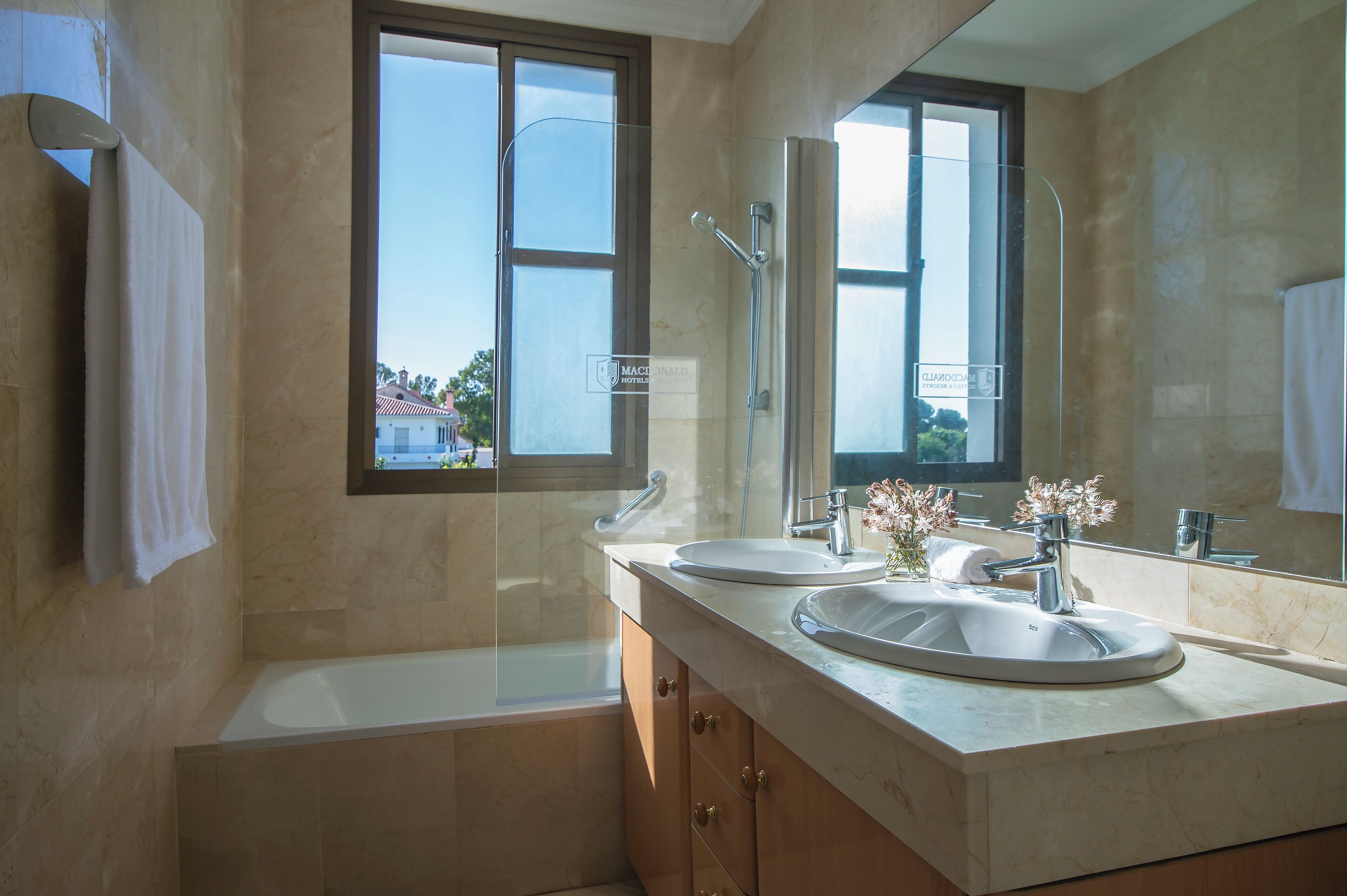 A bathroom with two sinks, a bathtub, and a large mirror reflecting a window.