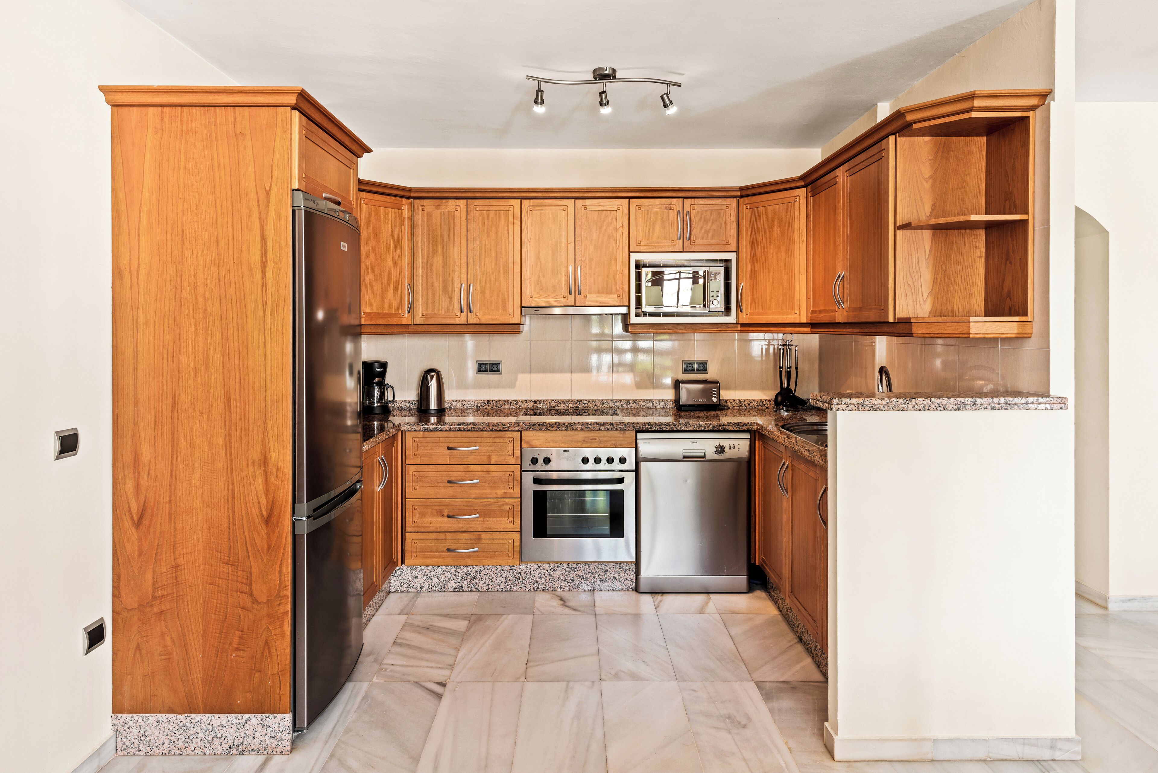 A kitchen with wooden cabinets, stainless steel appliances, granite countertops, and a tiled floor.