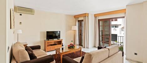 A modern living room with a sofa set, a coffee table, a flat-screen TV, and a balcony with a view.