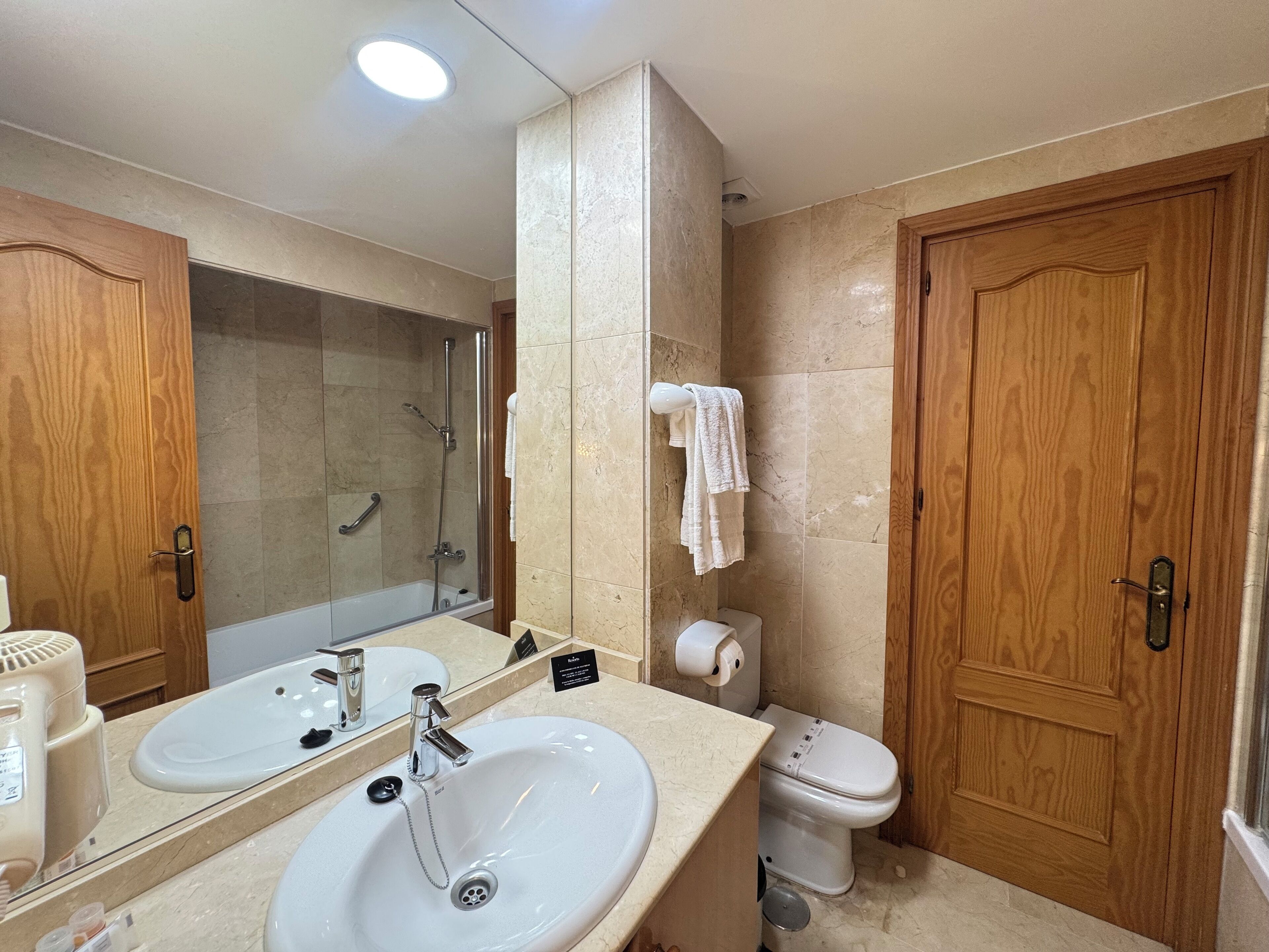Een badkamer met een wastafel, spiegel, douche, toilet en houten deuren.