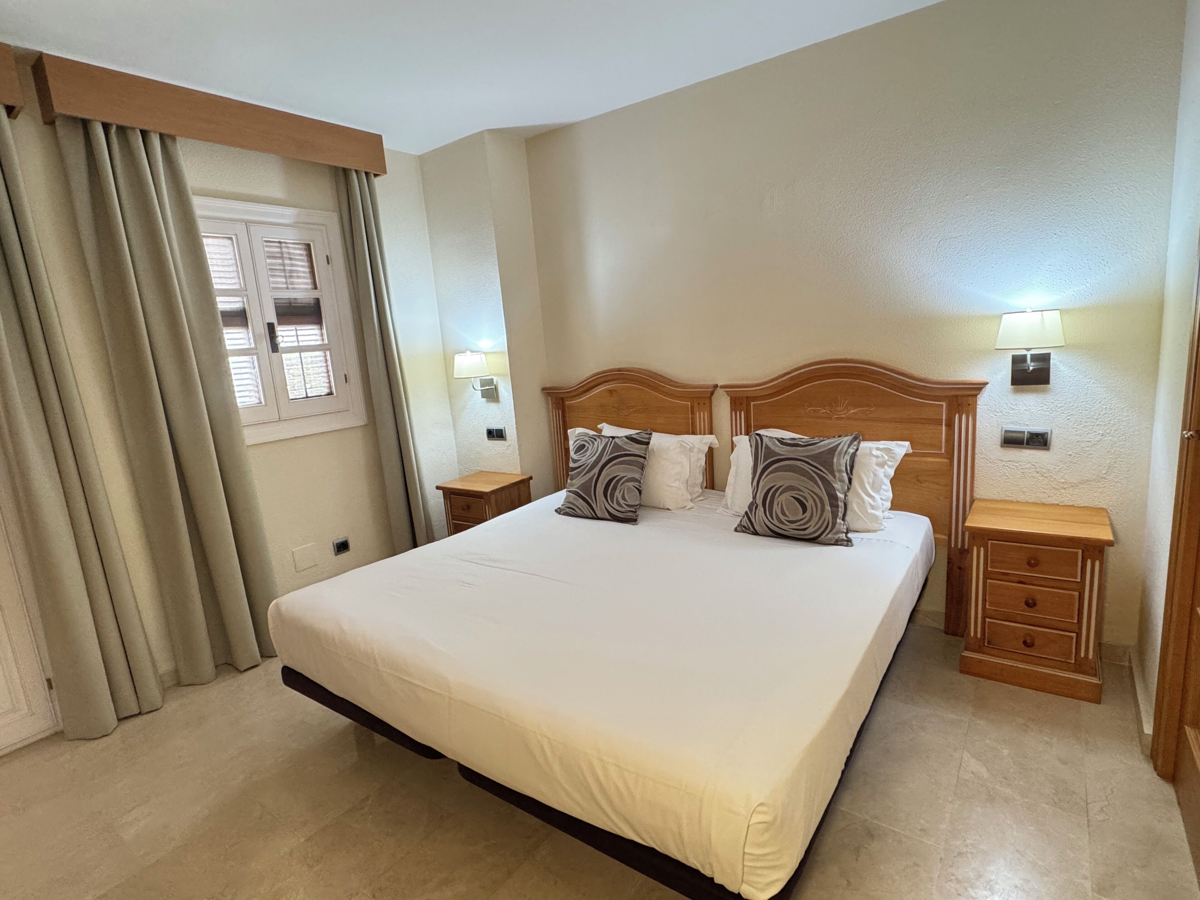 Una camera da letto con un letto grande, una testiera in legno, due comodini e una finestra con tende.