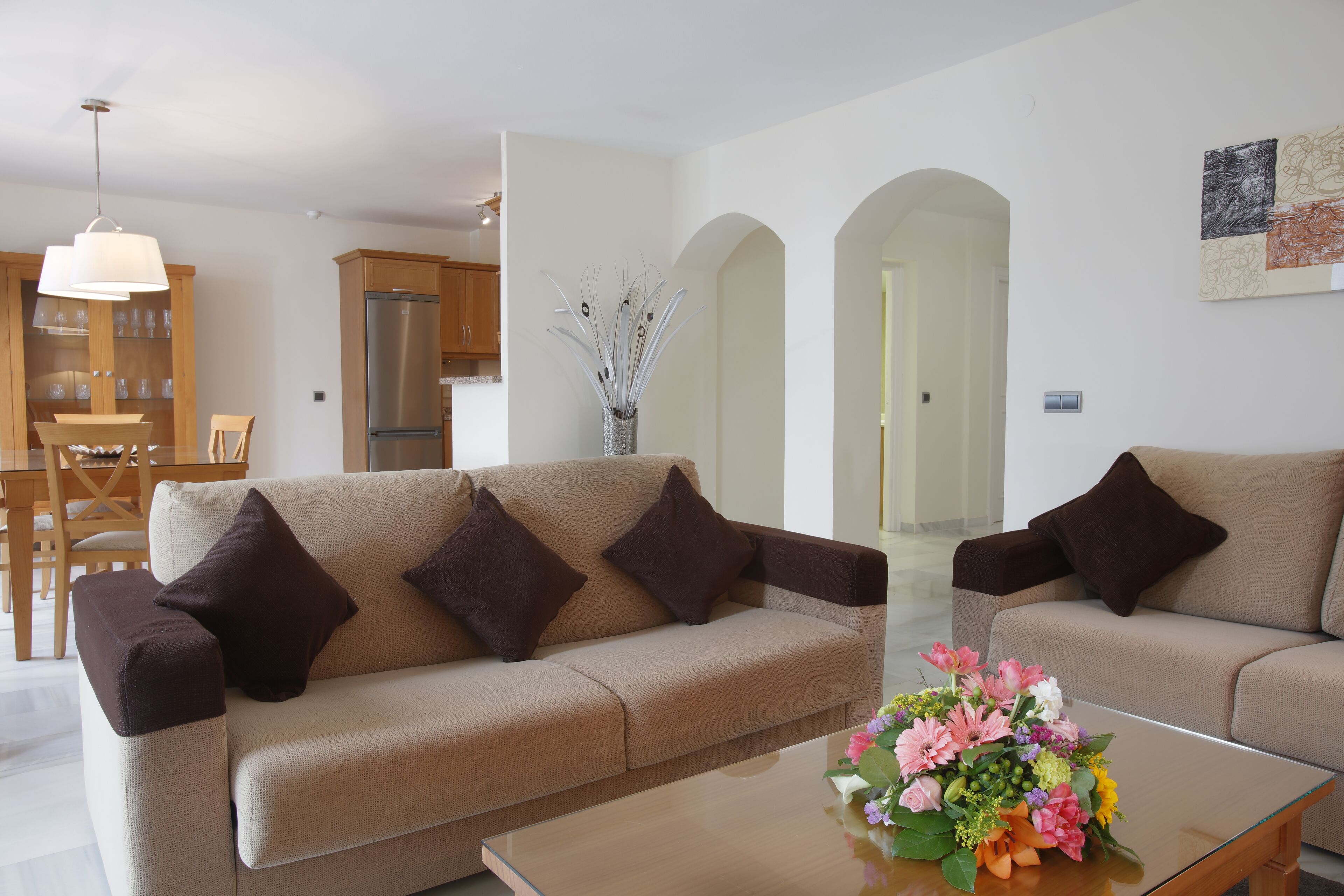 A living room with two sofas, a coffee table, and a dining area with wooden furniture.