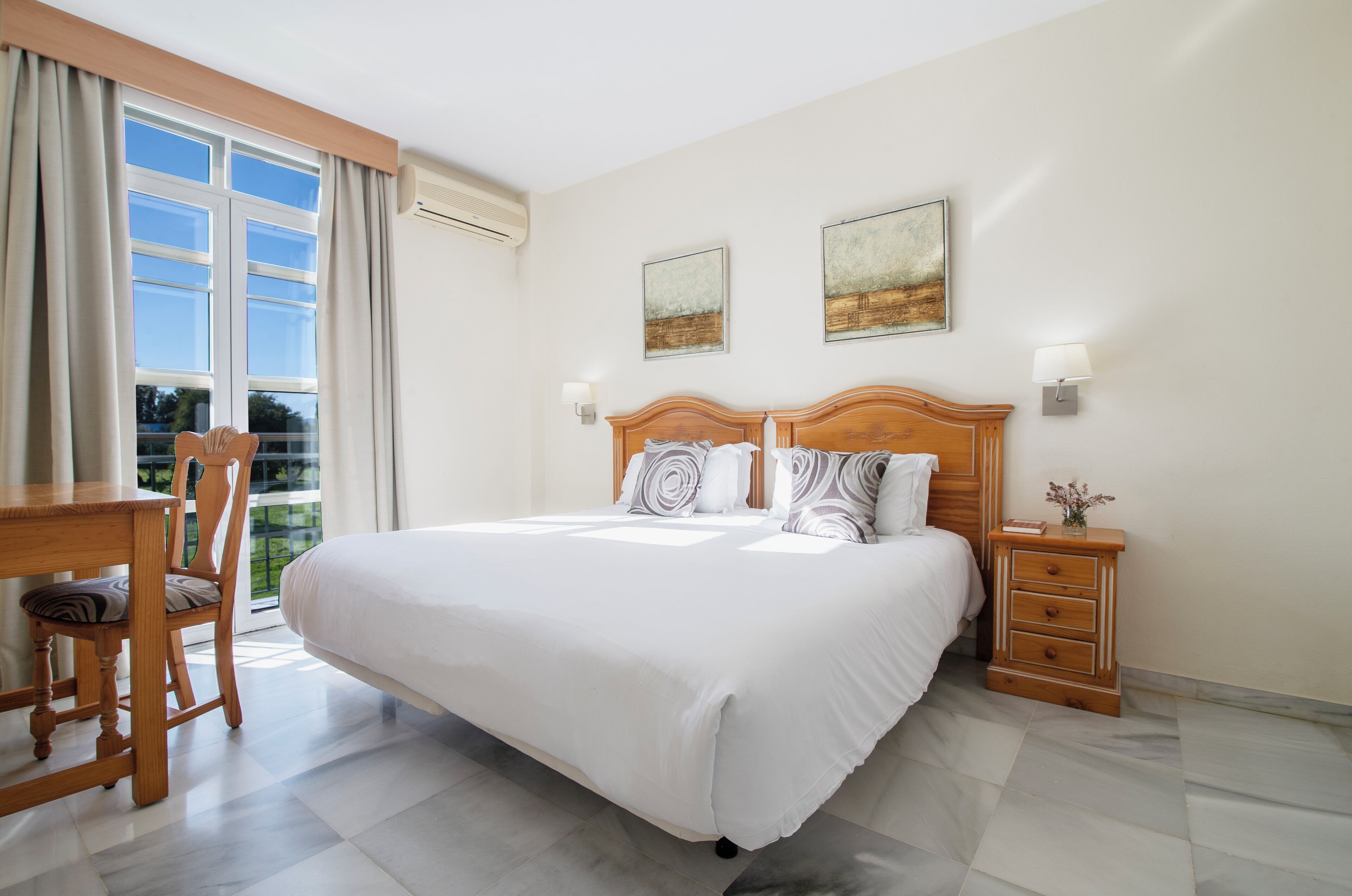 Une chambre à coucher avec un grand lit, une tête de lit en bois, deux lampes fixées au mur et une petite table de chevet avec une lampe.