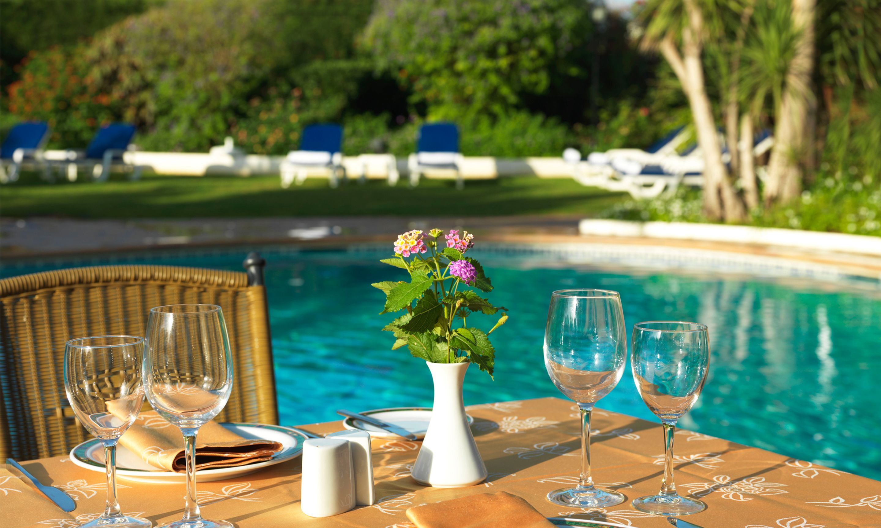 A dining table with a vase of flowers, wine glasses, and cutlery.