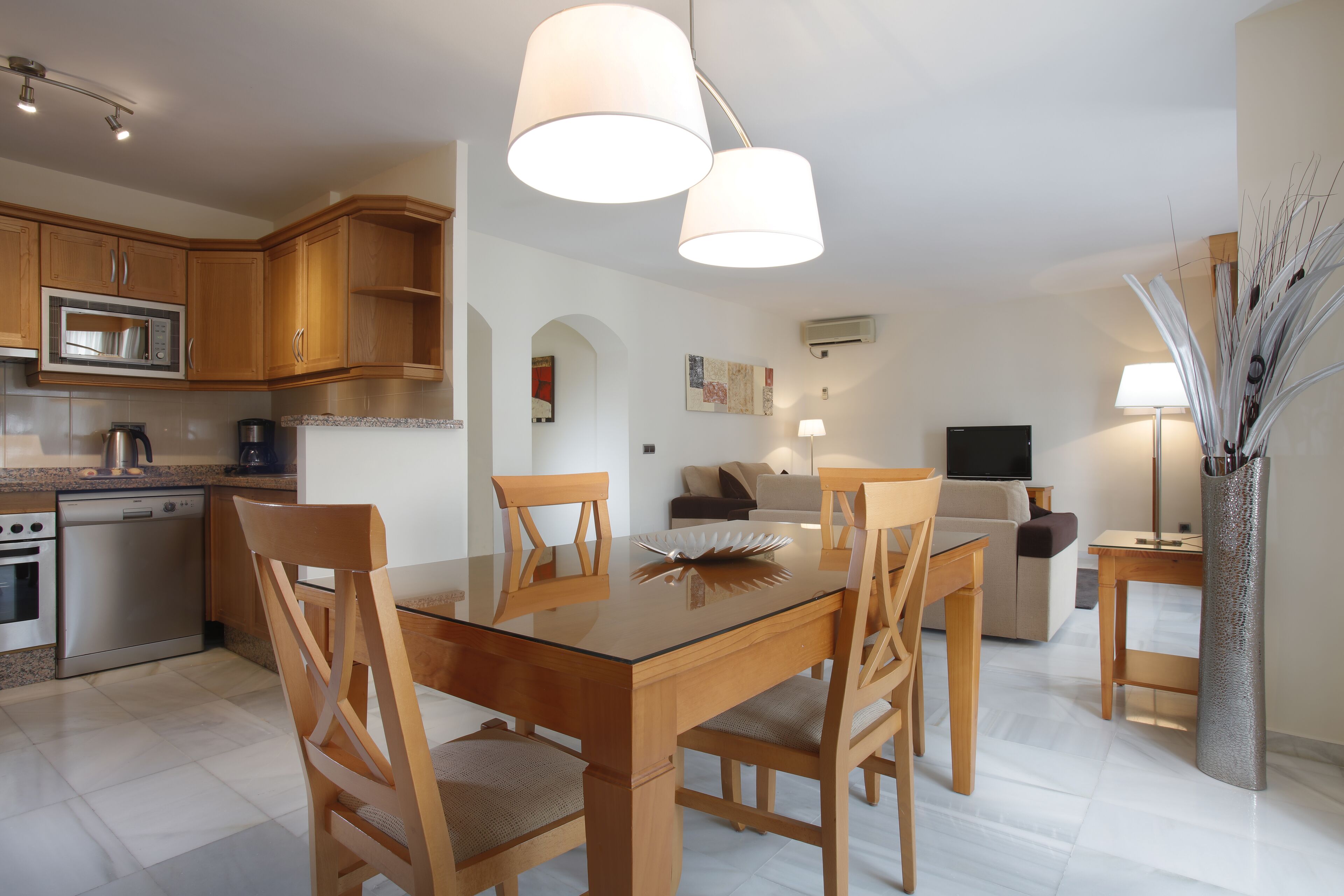 A modern kitchen with wooden cabinets, a stainless steel microwave, and a glass dining table with chairs.