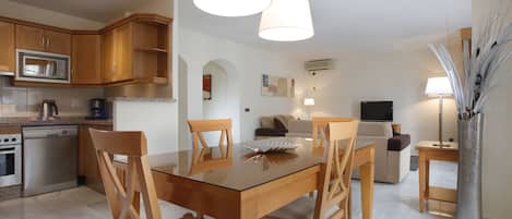 A modern kitchen with wooden cabinets, a stainless steel microwave, and a glass dining table with chairs.