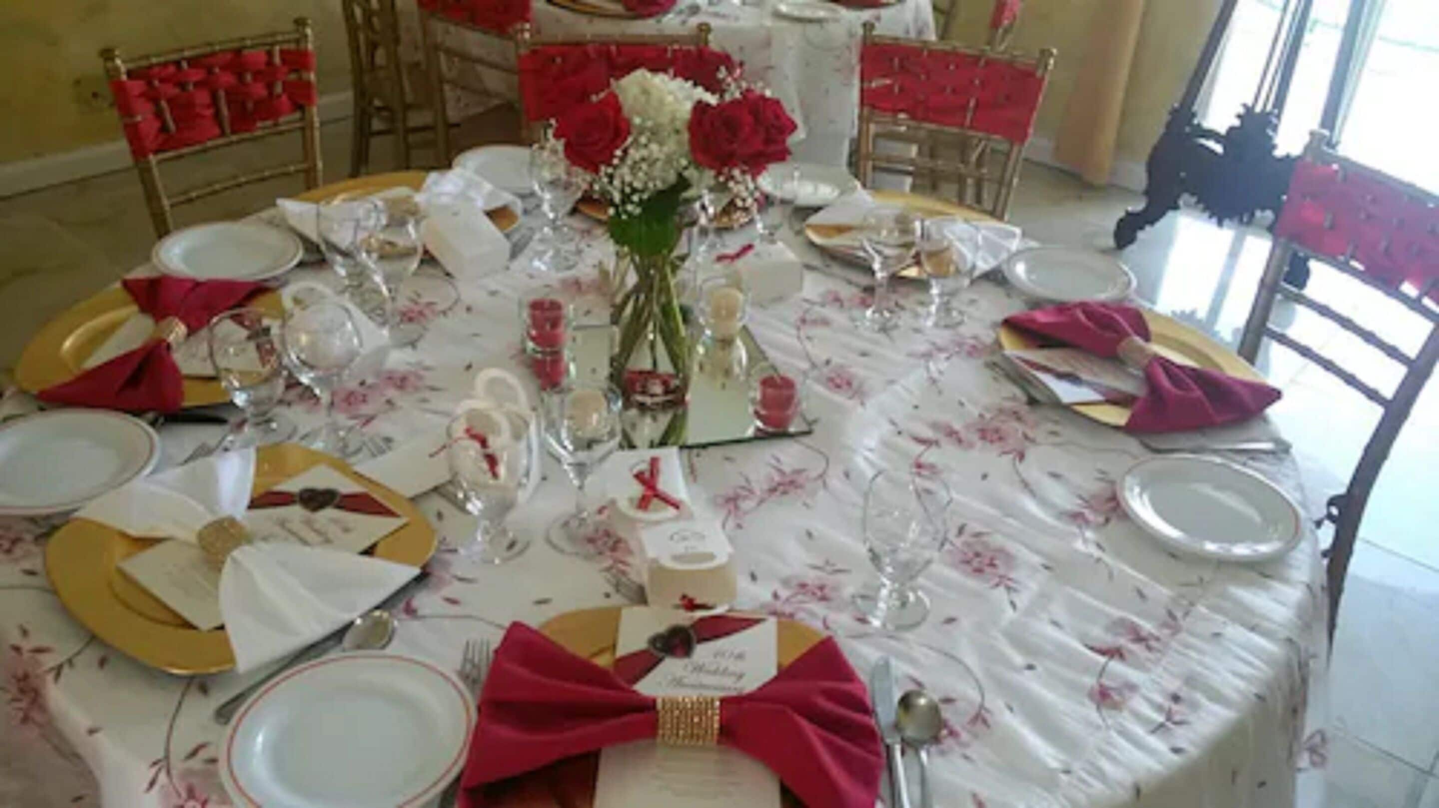 Une table ronde dressée pour un événement formel, avec une nappe blanche, des serviettes rouges et des décorations florales.