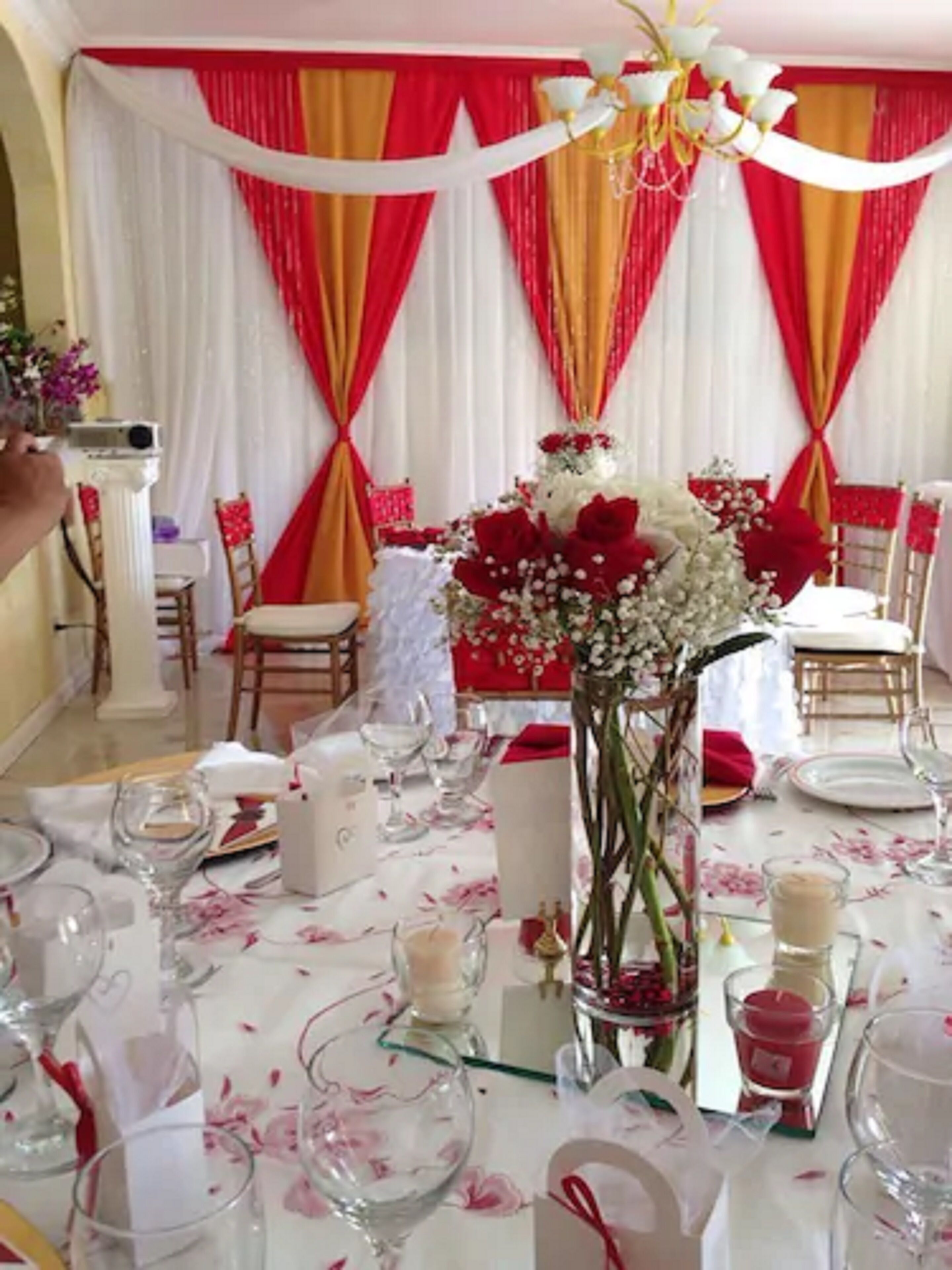 Zona de dinar amb taules preparades per a un esdeveniment formal, amb cortines vermelles i blanques, centrals florals i tovallons blancs.