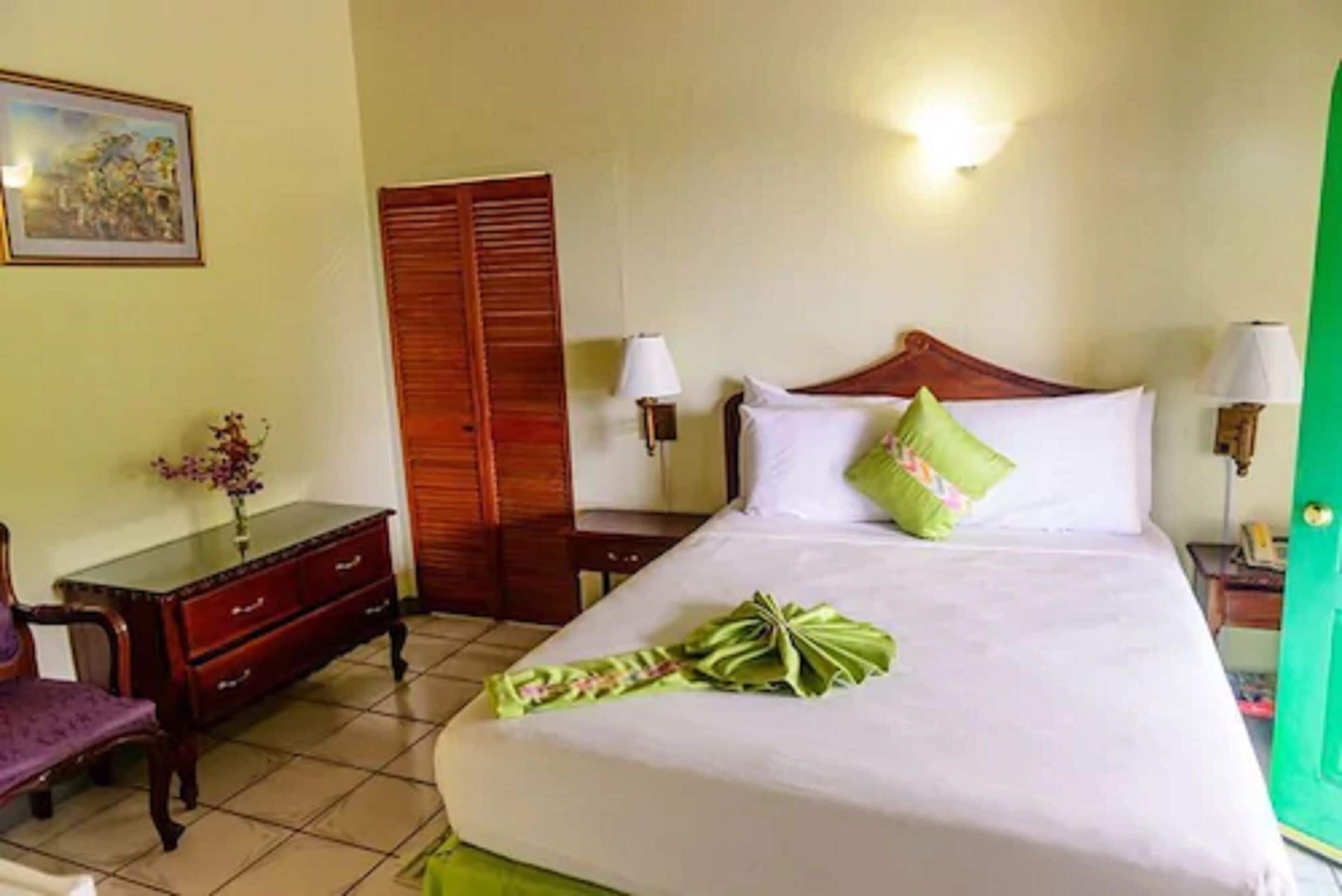 Een hotelkamer met een bed, een houten garderobe, een bureau met een lamp en een stoel.