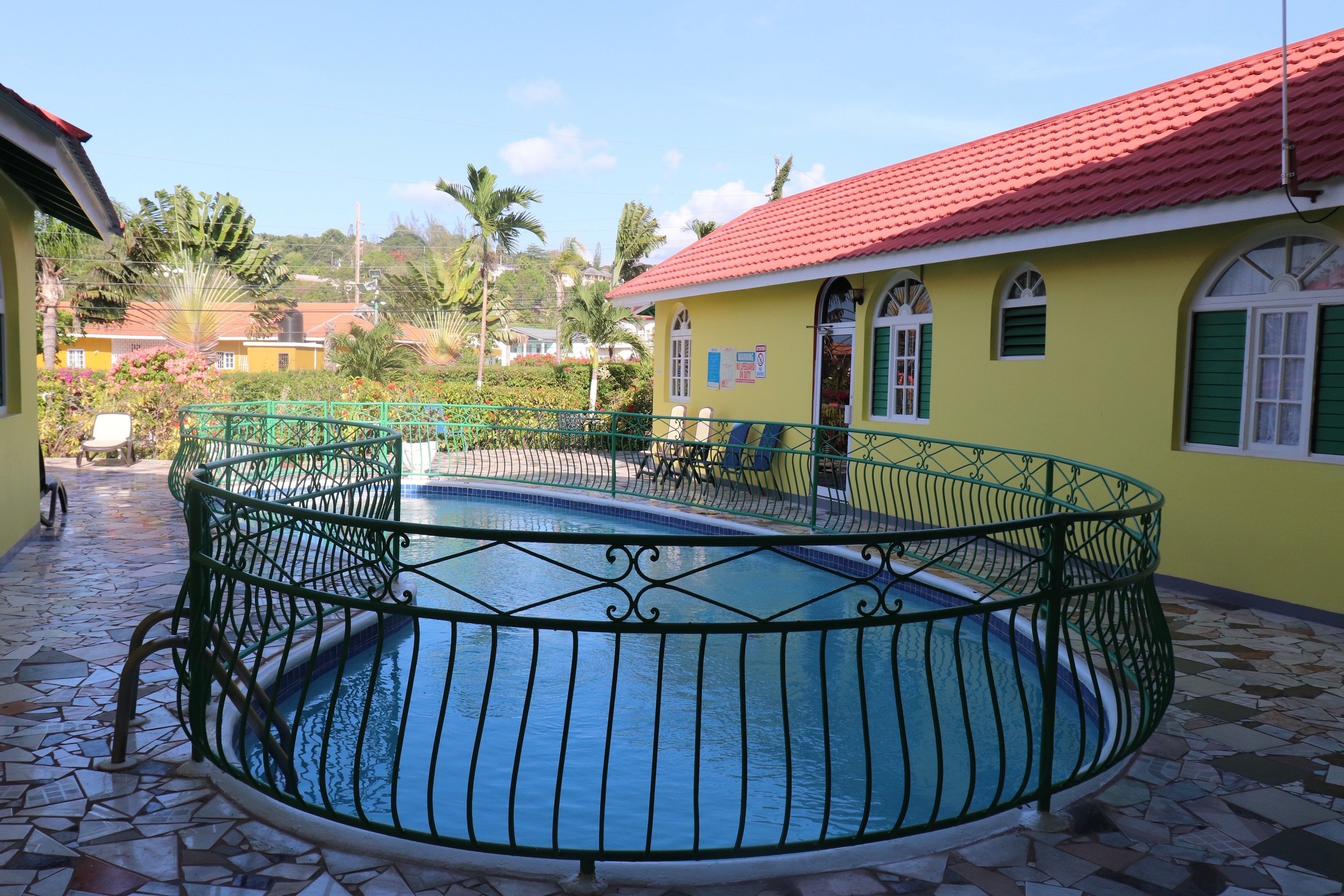 A circular pool with a green metal railing, surrounded by a tiled patio.