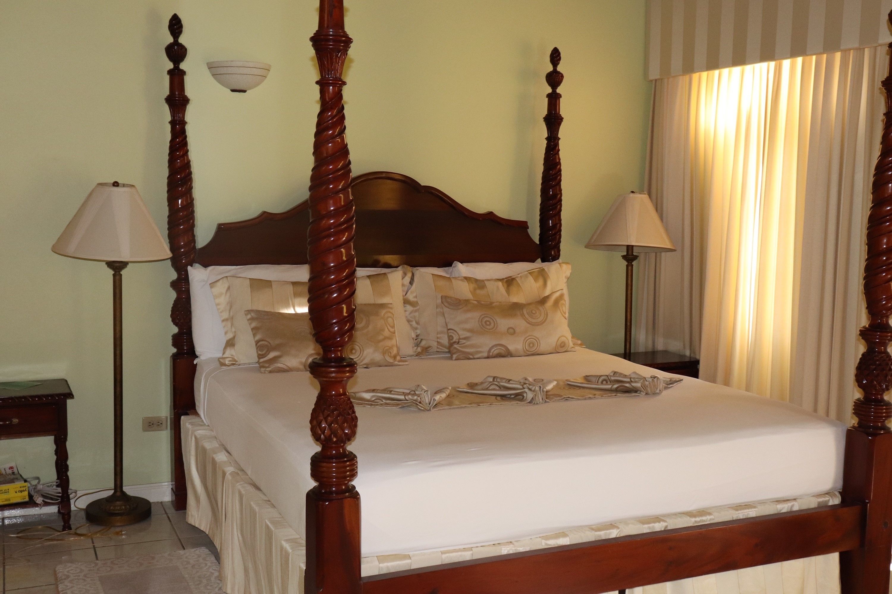 A four-poster bed with a wooden headboard, two bedside lamps, and a window with curtains.