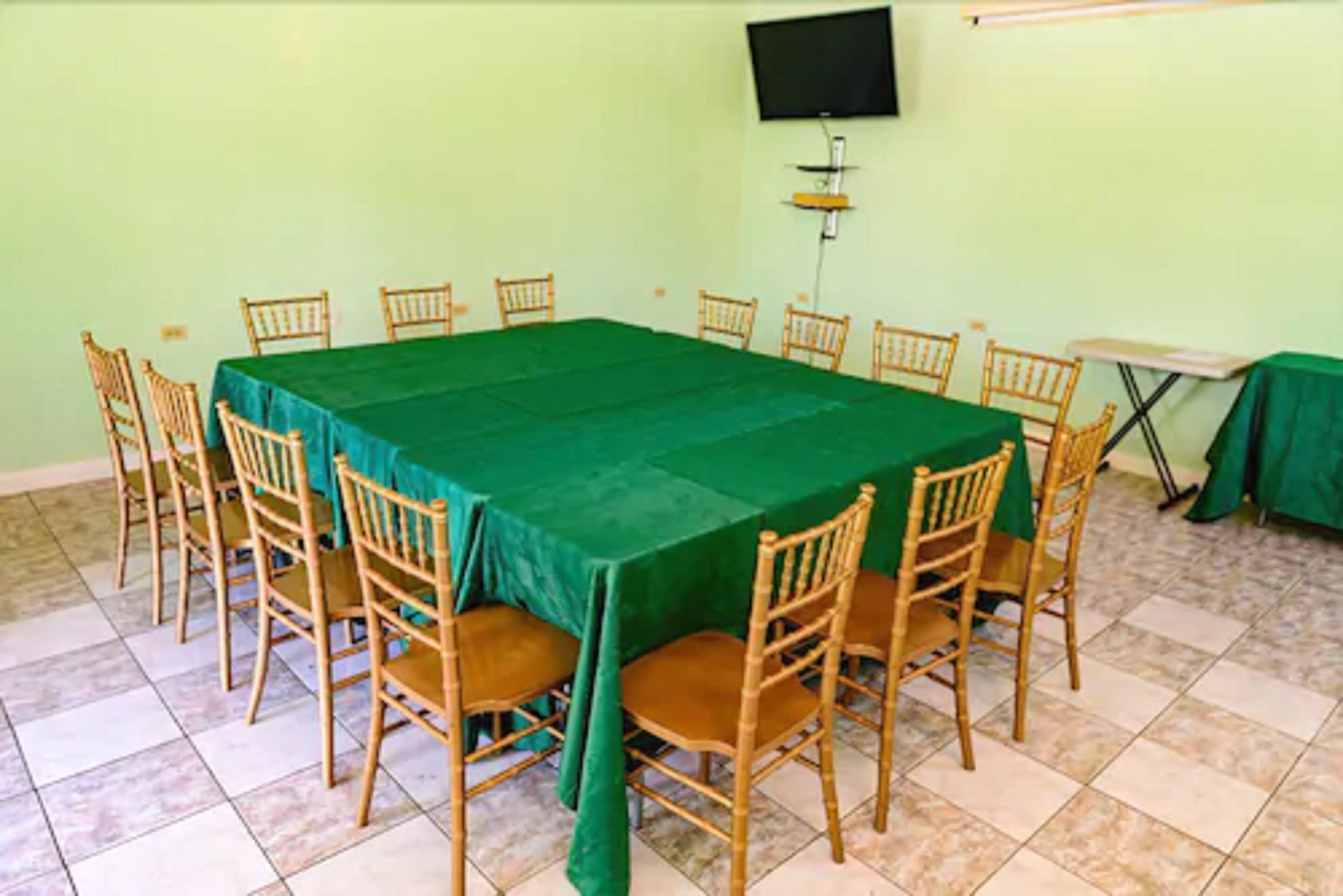 Una sala de conferencias con una mesa verde, sillas de madera, un televisor en la pared y suelo de baldosas.
