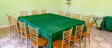 Una sala de conferencias con una mesa verde, sillas de madera, un televisor en la pared y suelo de baldosas.