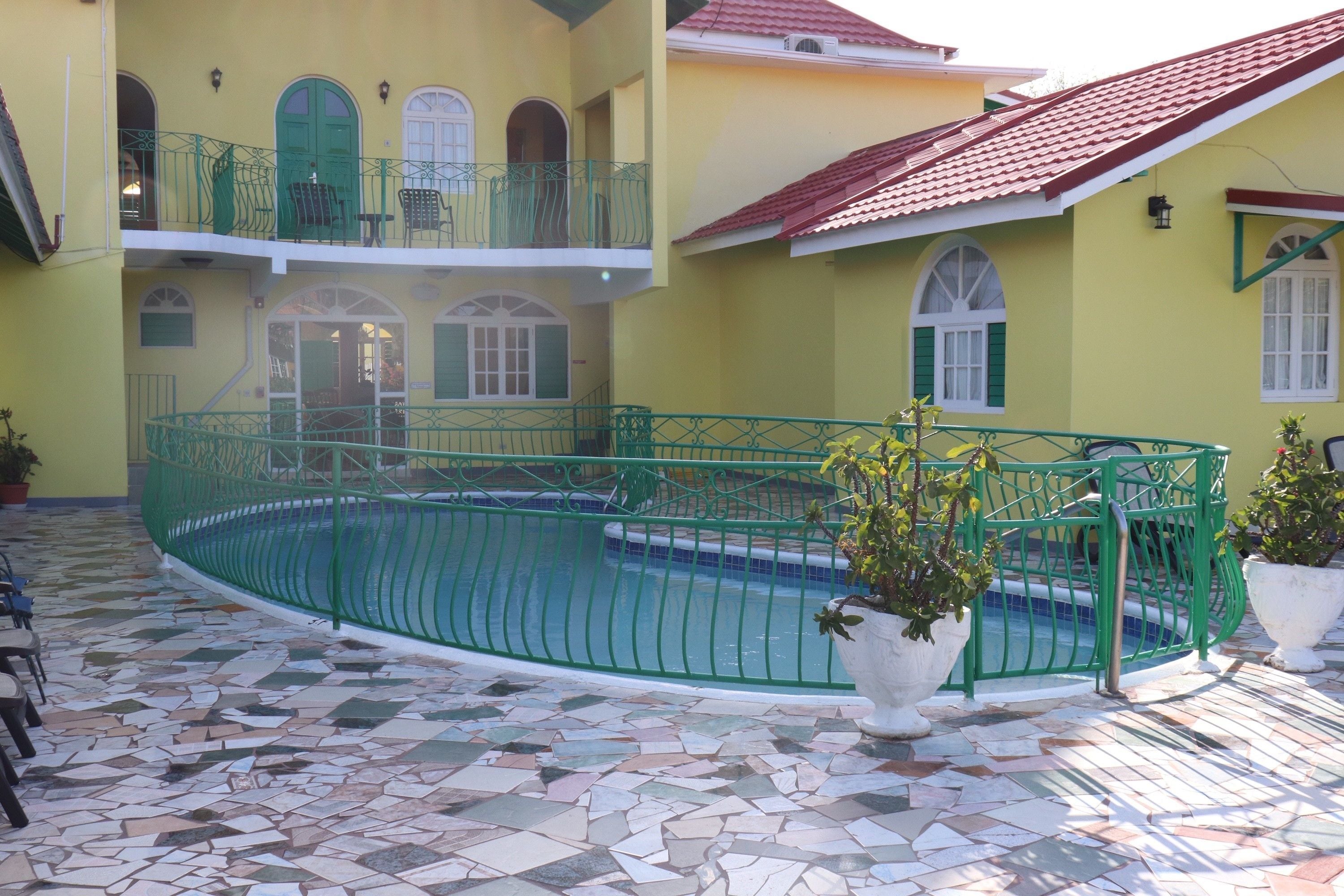 A pool area with a tiled floor, green railings, and potted plants.