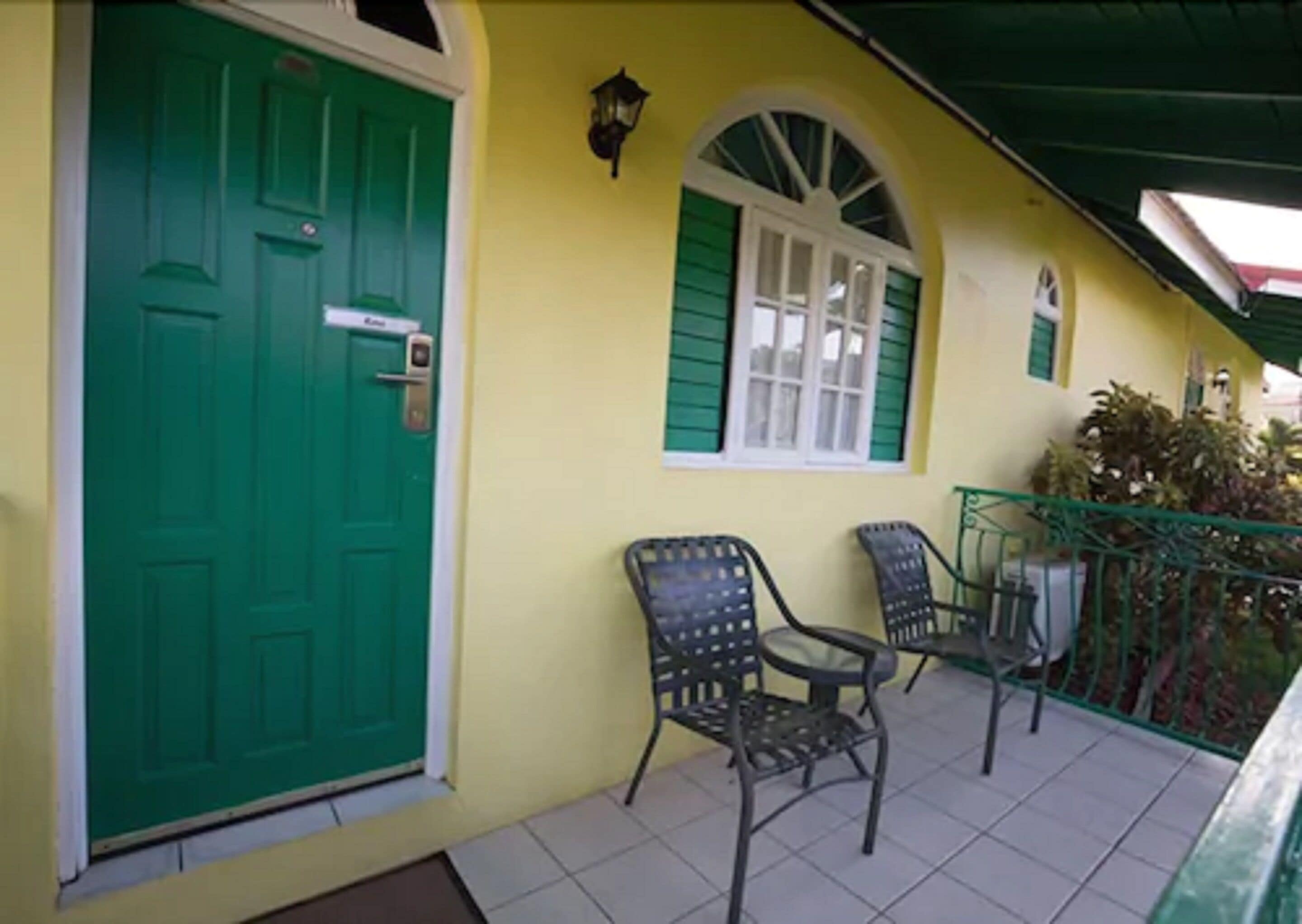 A yellow building with a green door, two chairs, and a window with green shutters.
