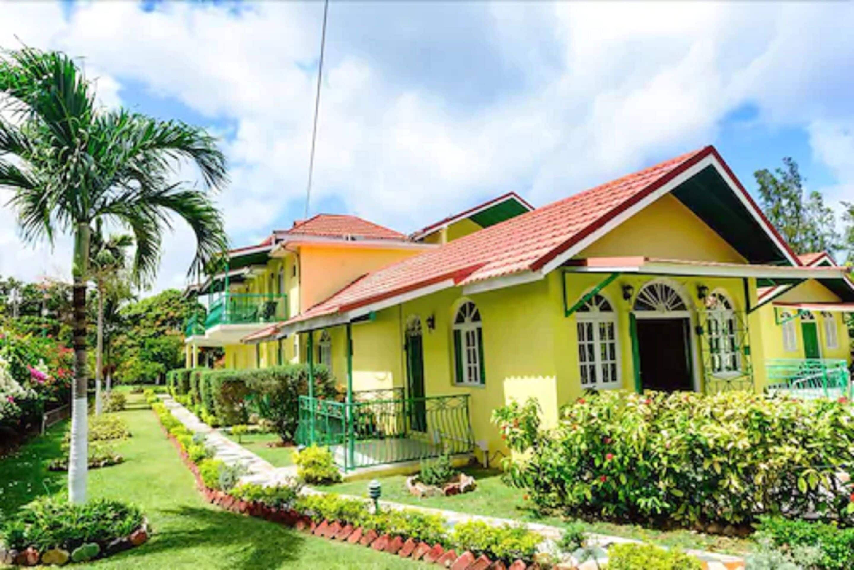 A two-story house with a red roof, green shutters, and a well-maintained garden.