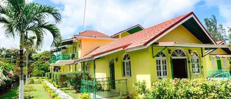 A two-story house with a red roof, green shutters, and a well-maintained garden.