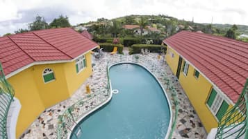 A pool area with two yellow buildings, each with a red roof, surrounded by a tiled deck.