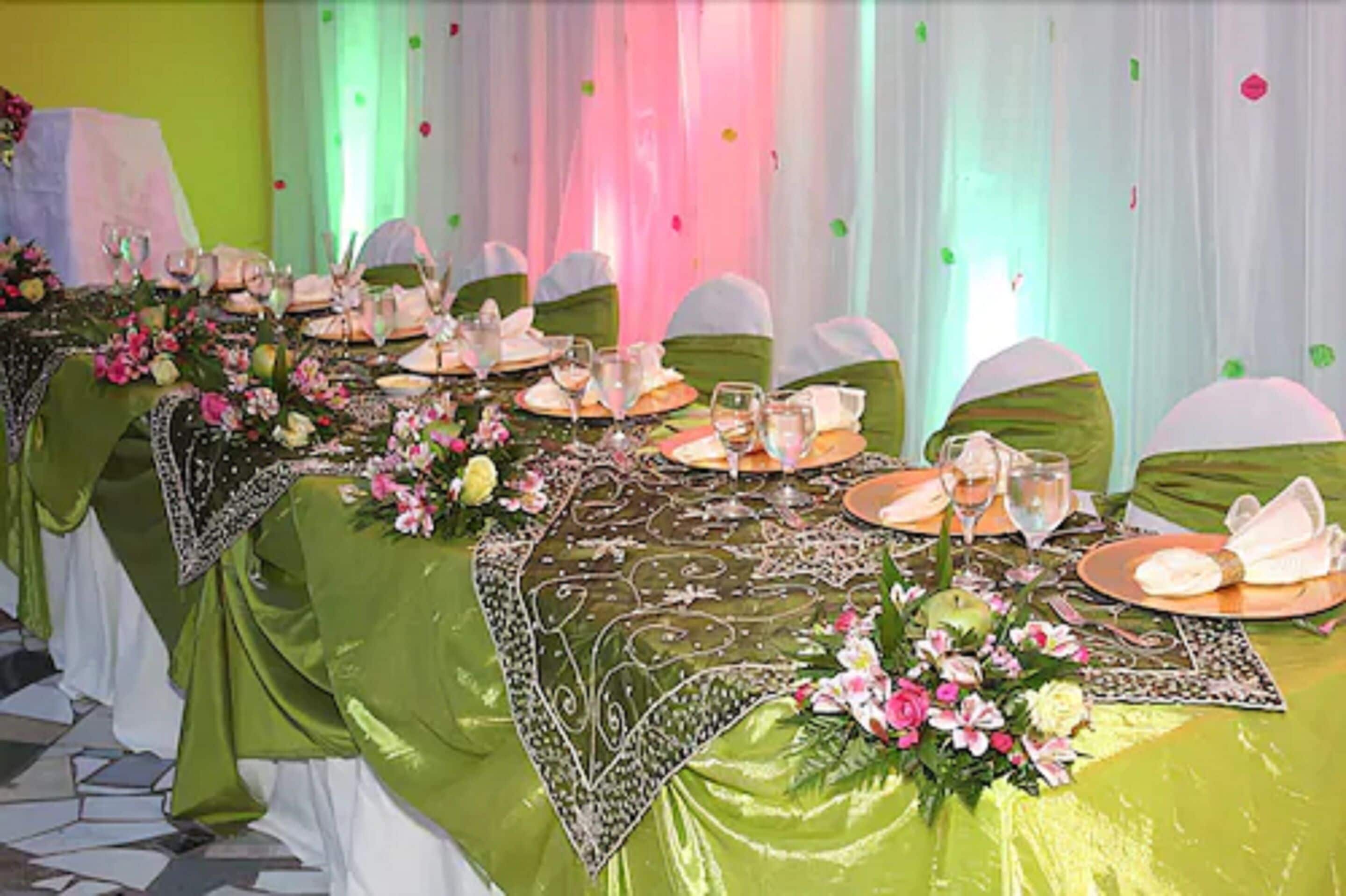 Ein festlich gedeckter Tisch mit grünen Tischdecken, weißen Stühlen und floralen Mittelpunkten.