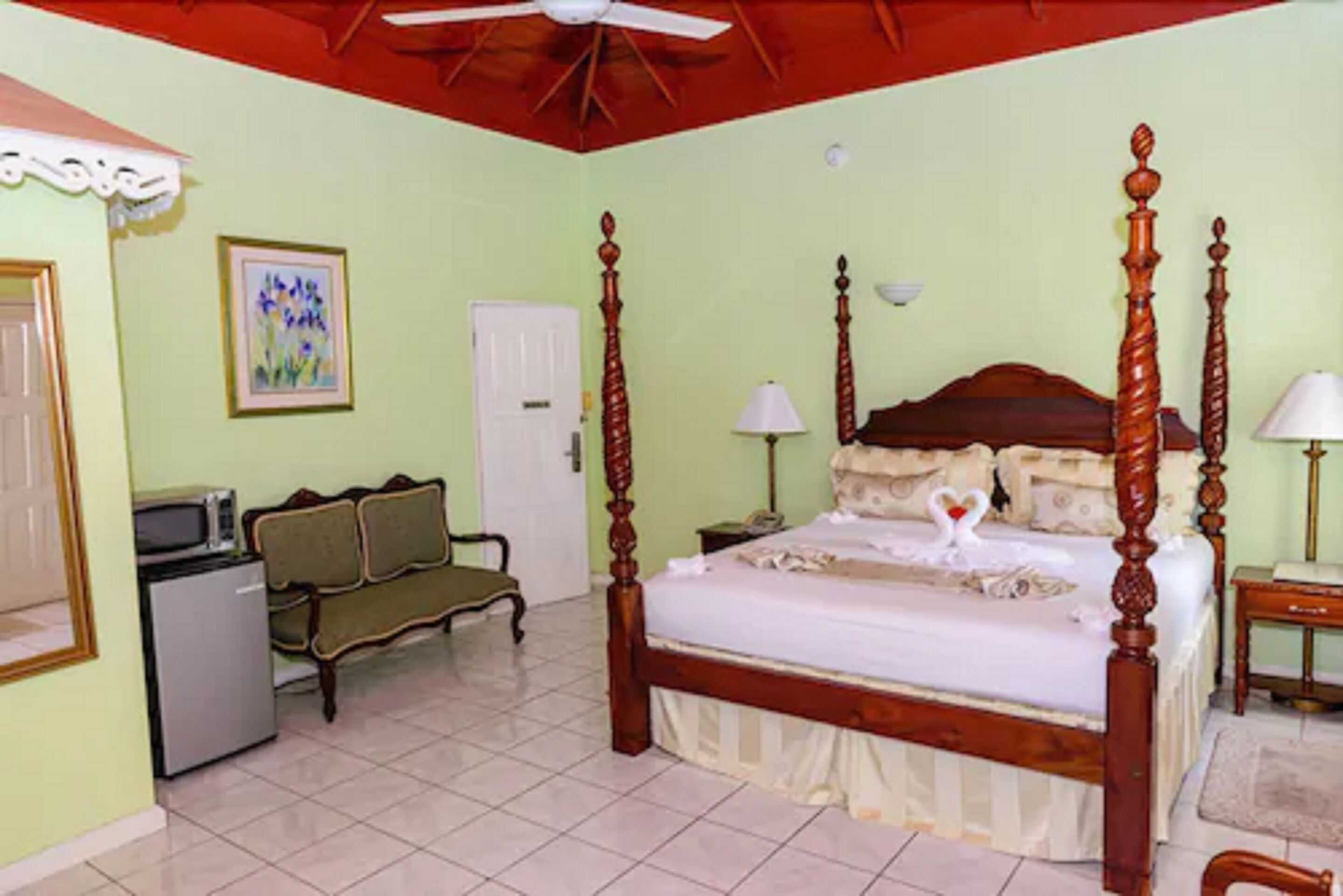 Une chambre à coucher avec un lit à baldaquin, un bureau avec une chaise, une télévision et un réfrigérateur.