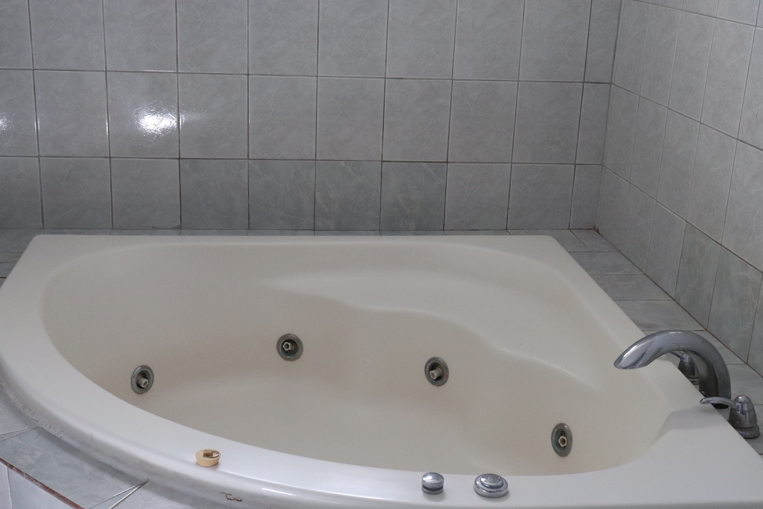 A large, rectangular bathtub with a single faucet and multiple drain holes.