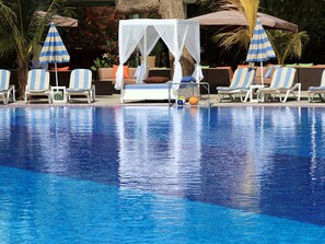 A swimming pool with lounge chairs and umbrellas, a canopy, and a palm tree. - Les Amaryllis Saly (Mbour)