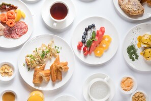 Verschiedene Frühstücksartikel wie Gebäck, Früchte und Getränke auf weißen Tellern.