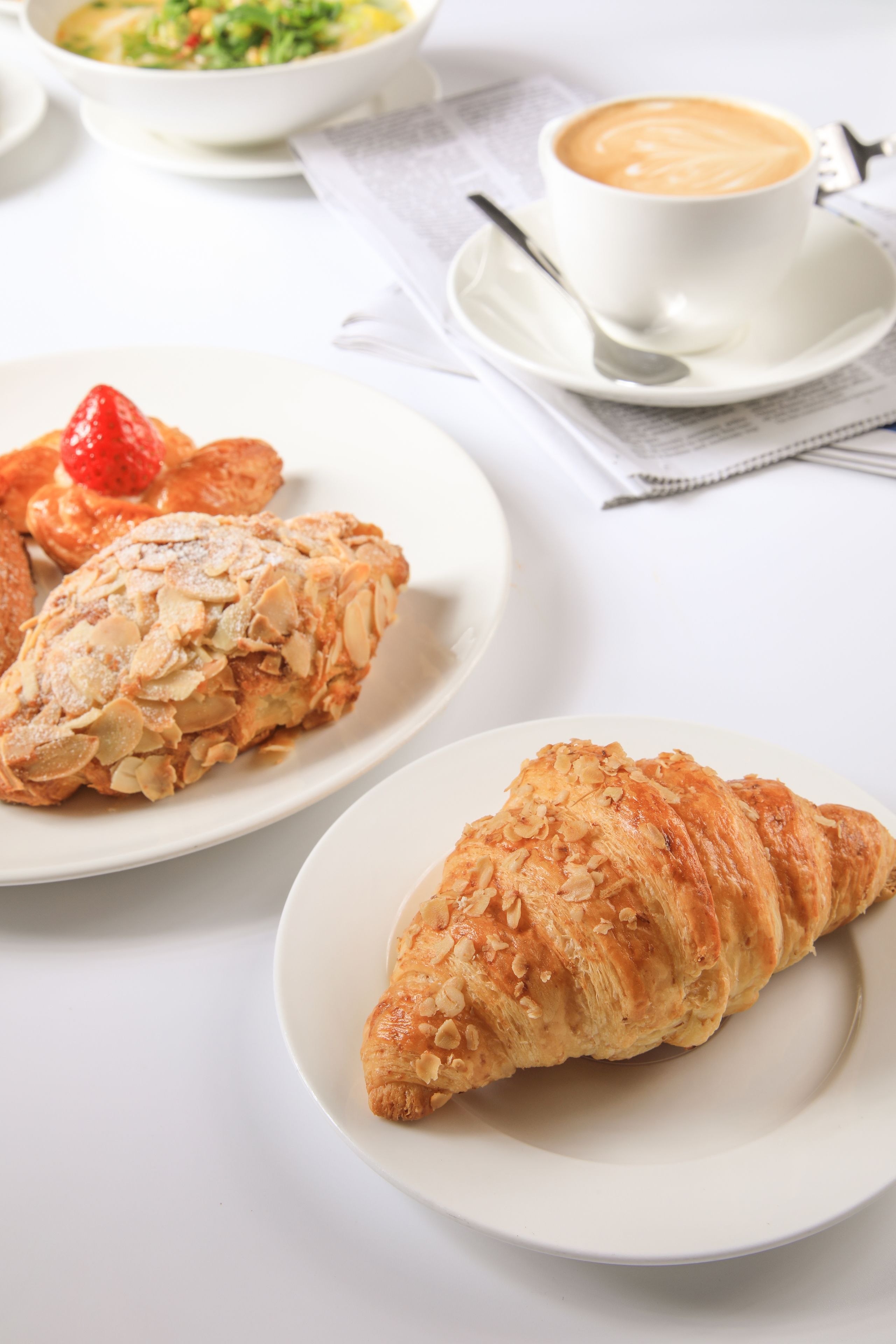 Una mesa con un croissant, un plato con una fresa y una taza de café.