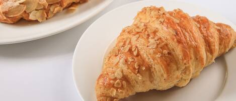 Una mesa con un croissant, un plato con una fresa y una taza de café.