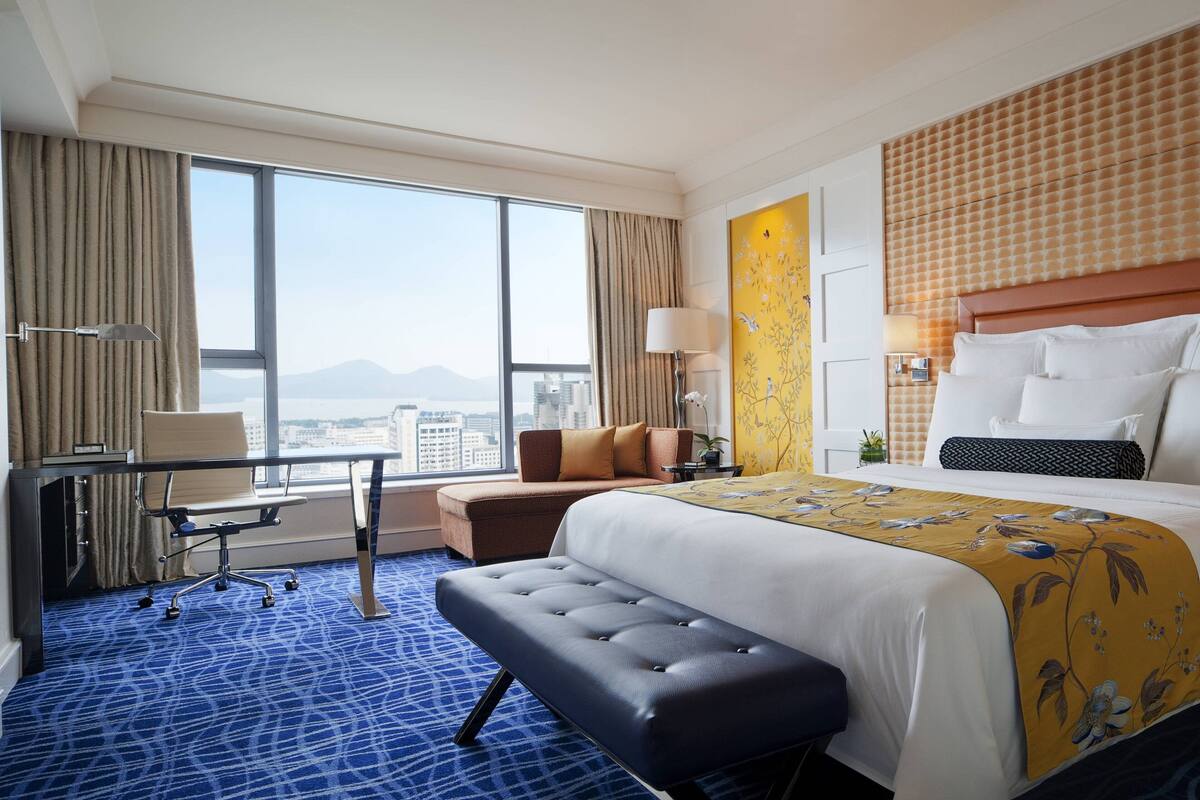Een hotelkamer met een groot bed, een bureau, een stoel en uitzicht op de stad.