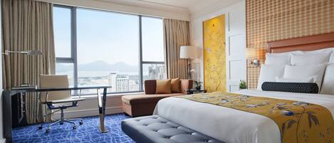 A hotel room with a large bed, a desk, a chair, and a view of the city.