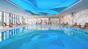 Een modern binnenzwembad met helderblauw water, ligbedden en een plafond met blauwe verlichtingsaccenten.