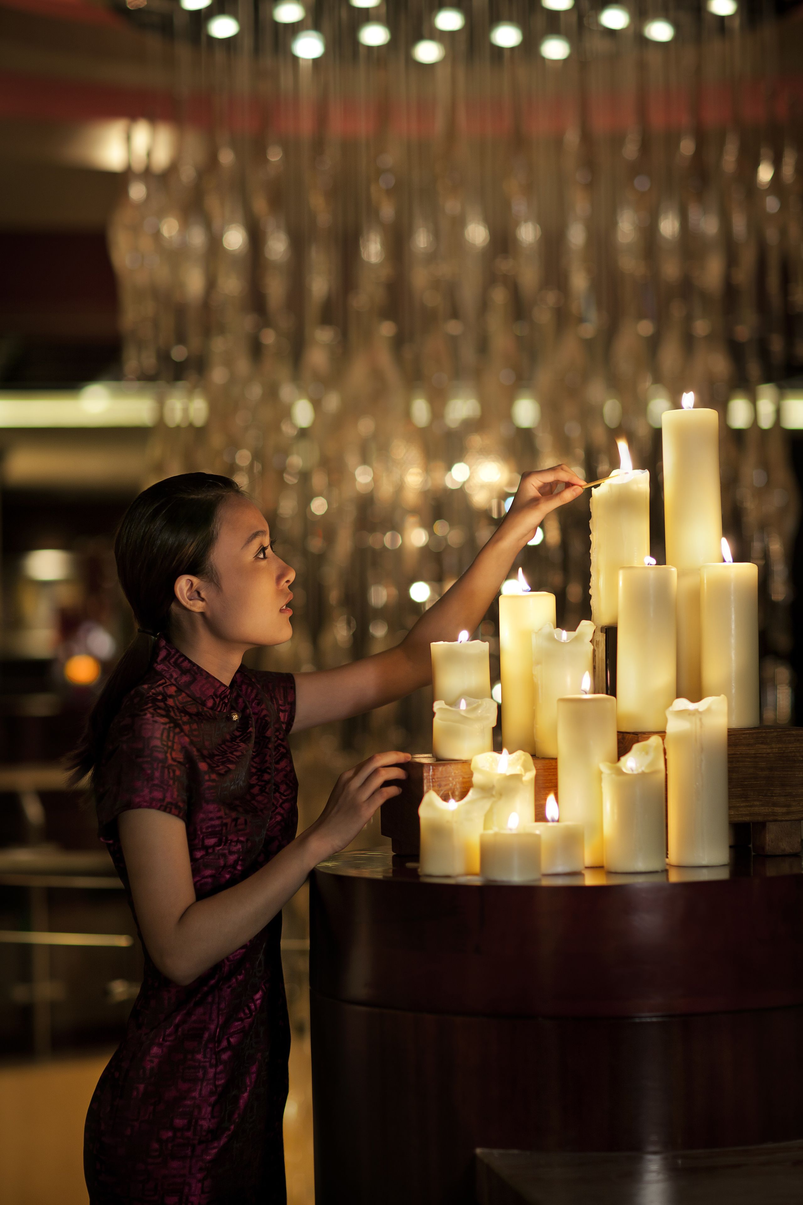 A person arranging candles in a dimly lit room with a patterned wall and a wooden counter.