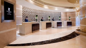 Een moderne hotel receptie met een vloer van gebogen marmer, een wand met ingelijste foto’s en een kroonluchter.
