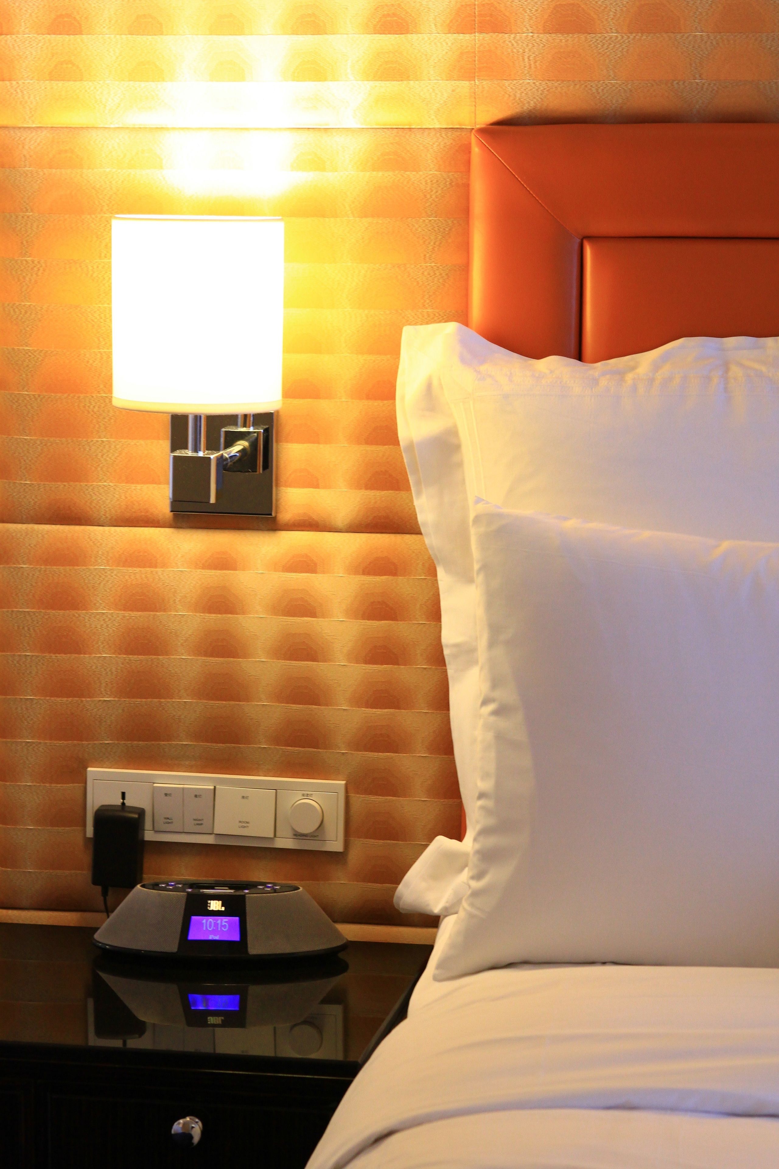 Een hotelkamer met een bed, een nachtkastje met een klok en een wandlamp.