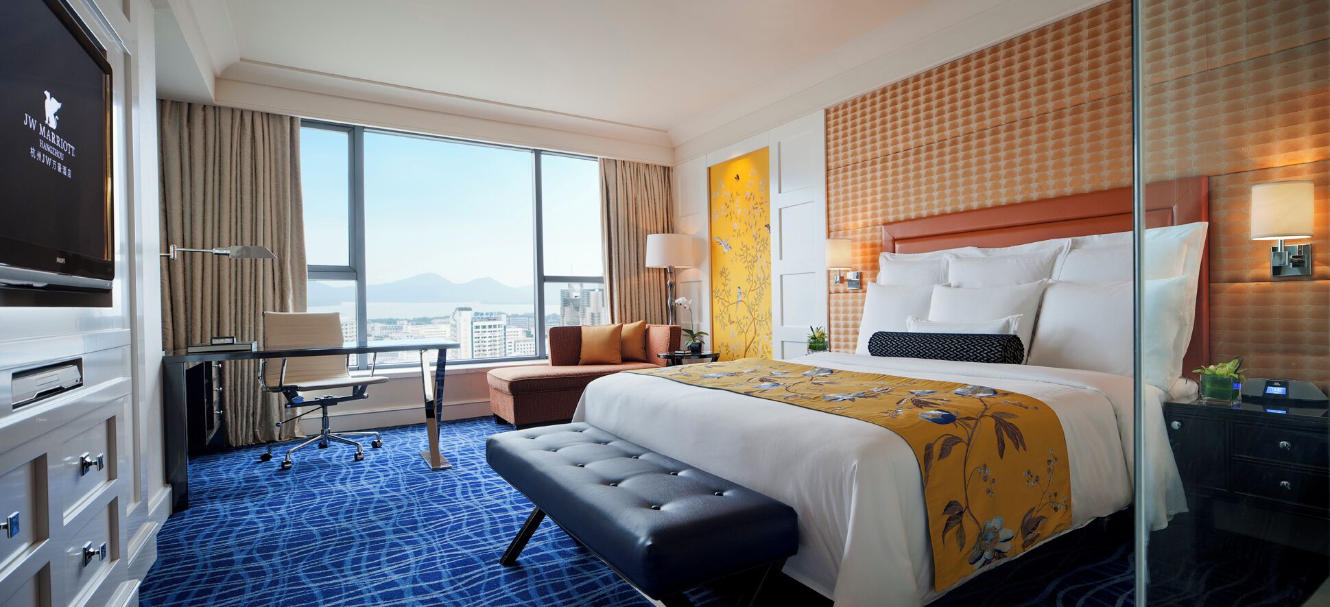 A hotel room with a large bed, a desk, a chair, and a television.