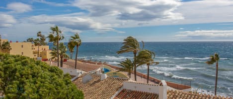 A coastal building with tiled roofs, palm trees, and a view of the ocean.