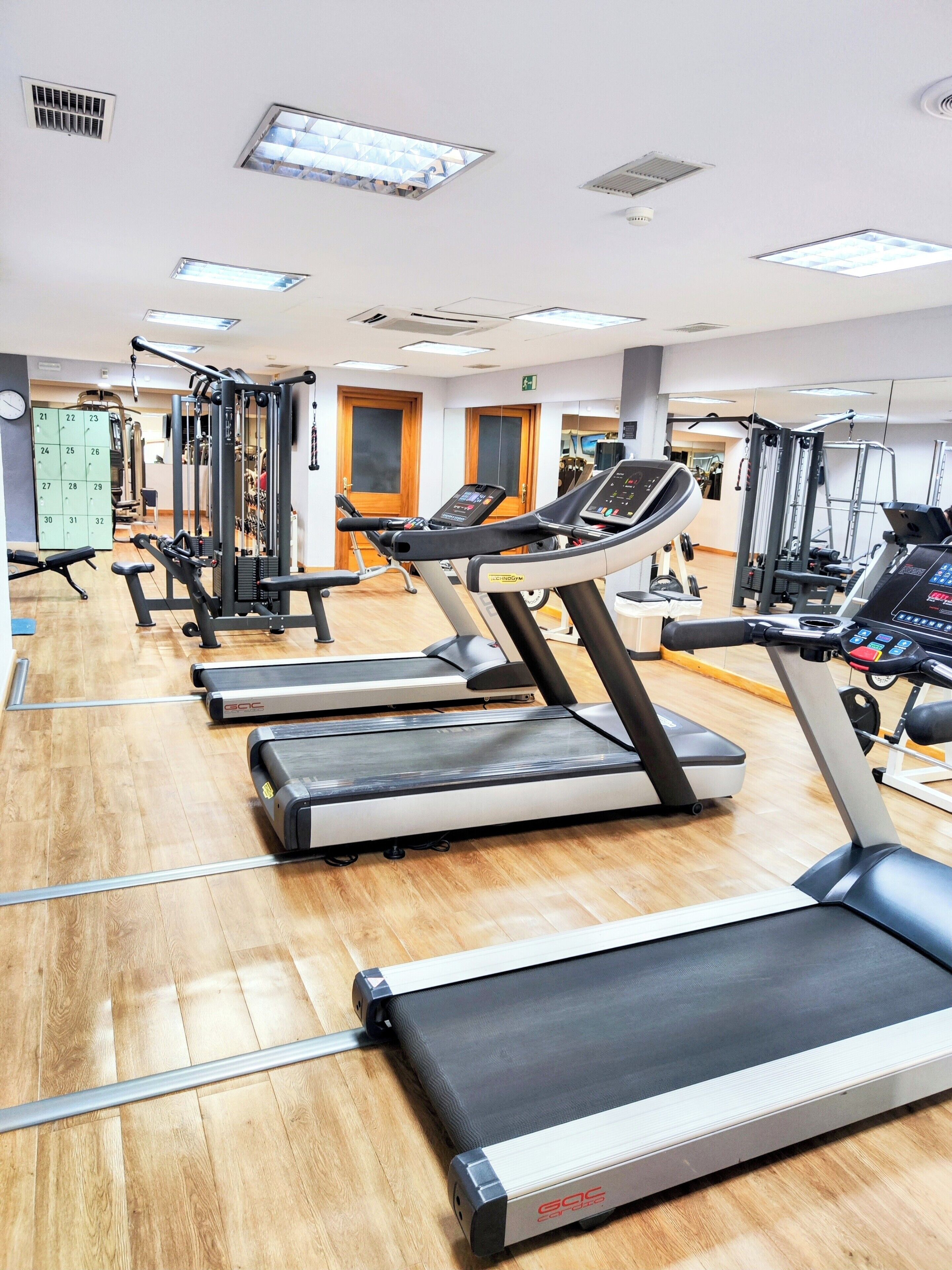 Une salle de sport équipée de tapis de course, d’appareils de musculation et d’un calendrier mural.
