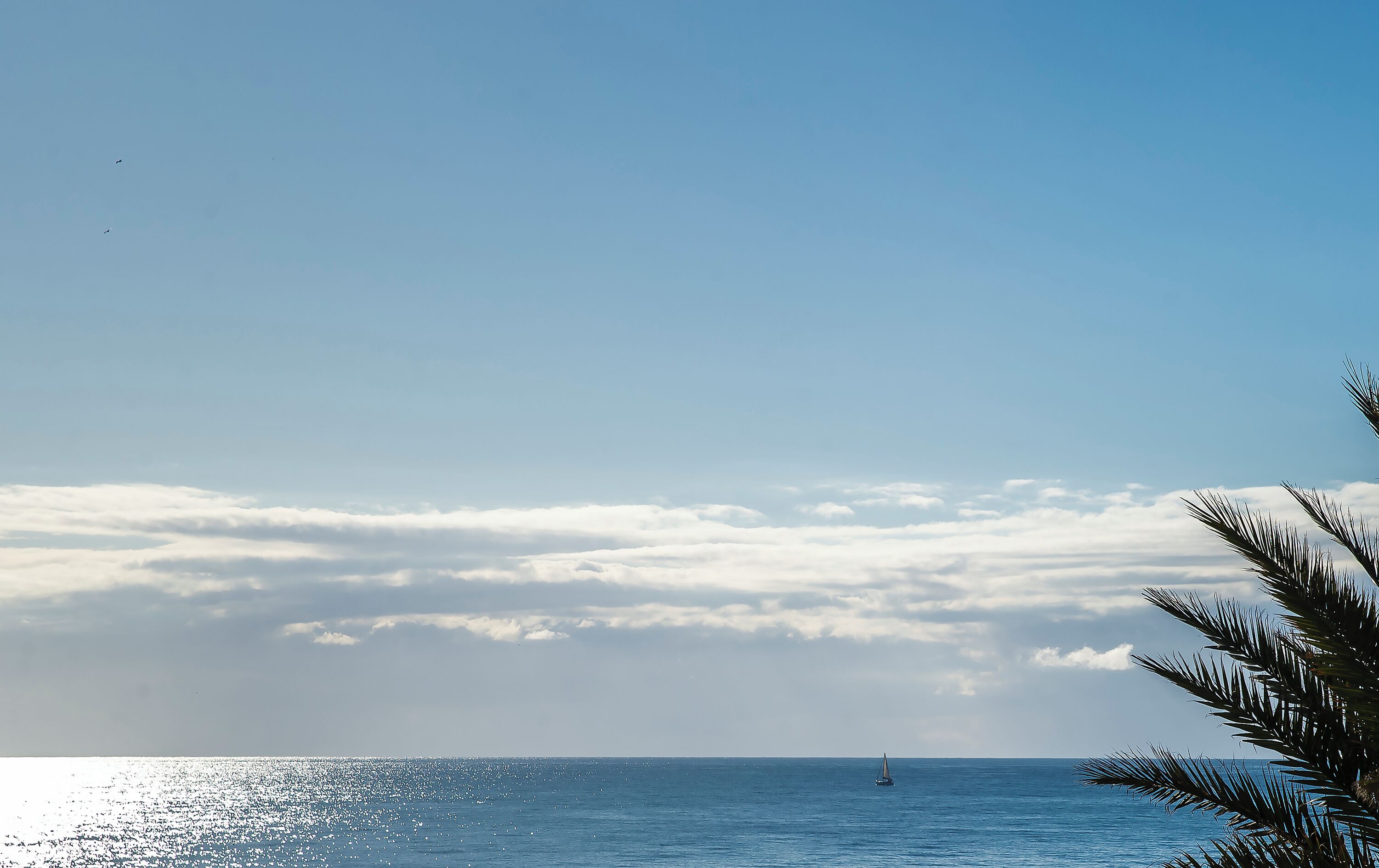 A clear sky with clouds, a calm sea, and a distant sailboat.