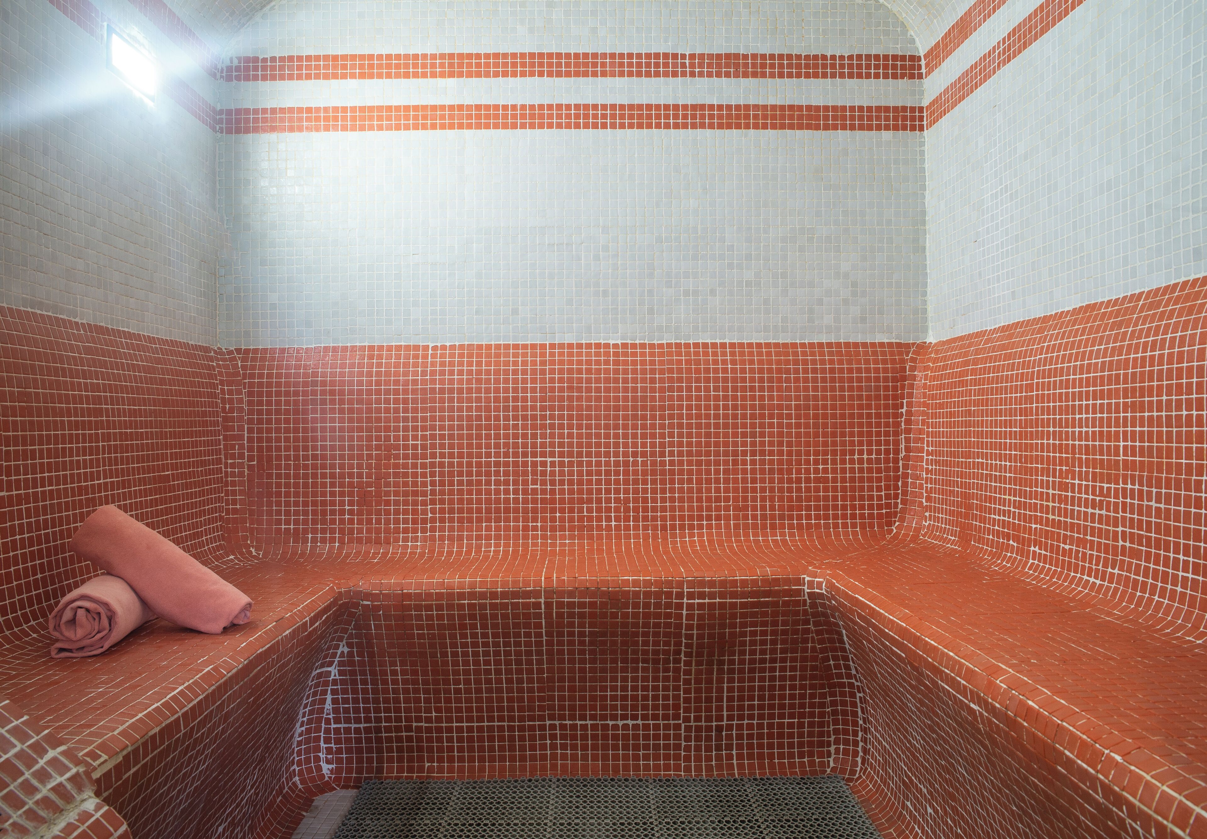 A tiled room with a bench and a rolled towel.