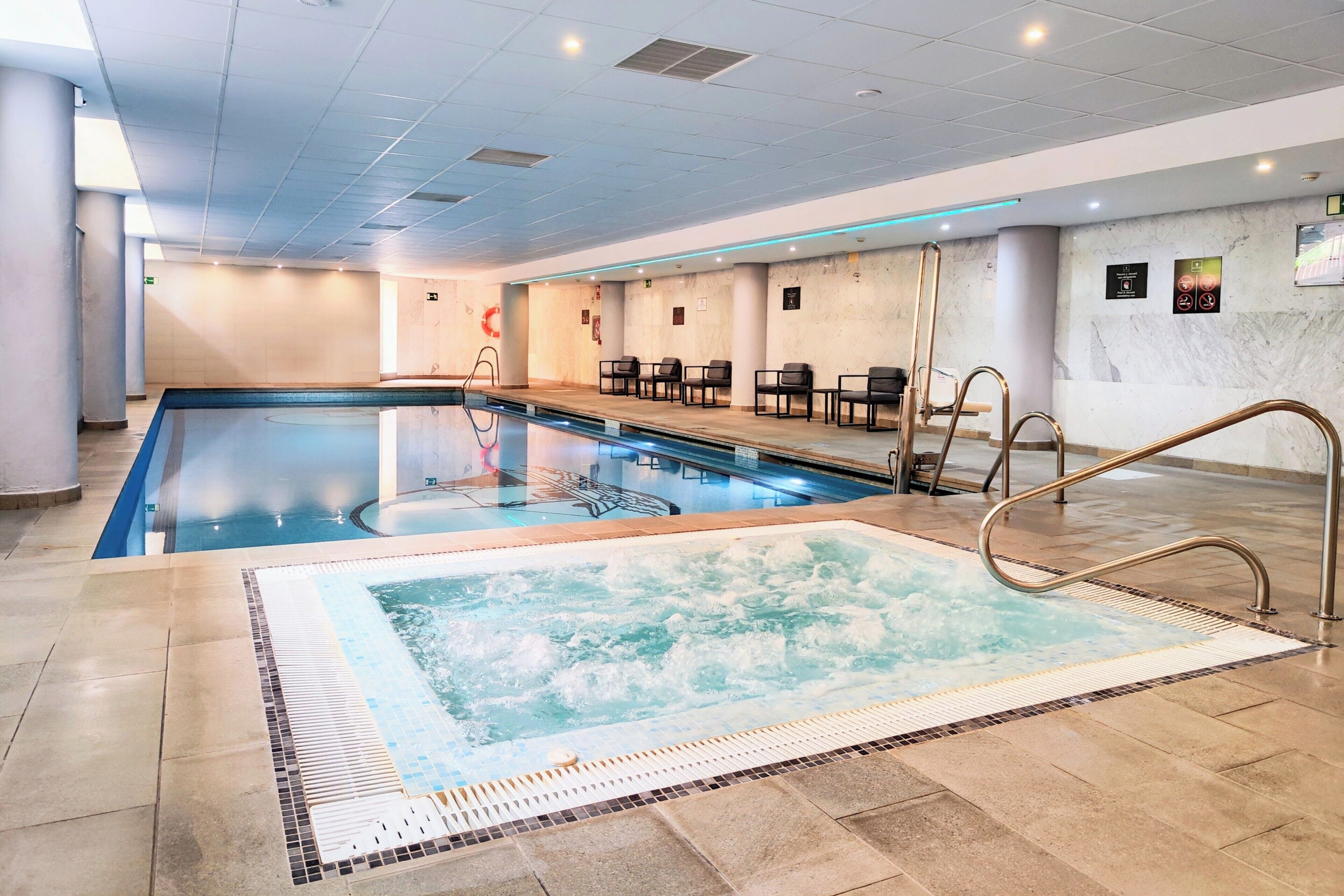 Una piscina con idromassaggio, pavimento piastrellato e area relax con sedie.