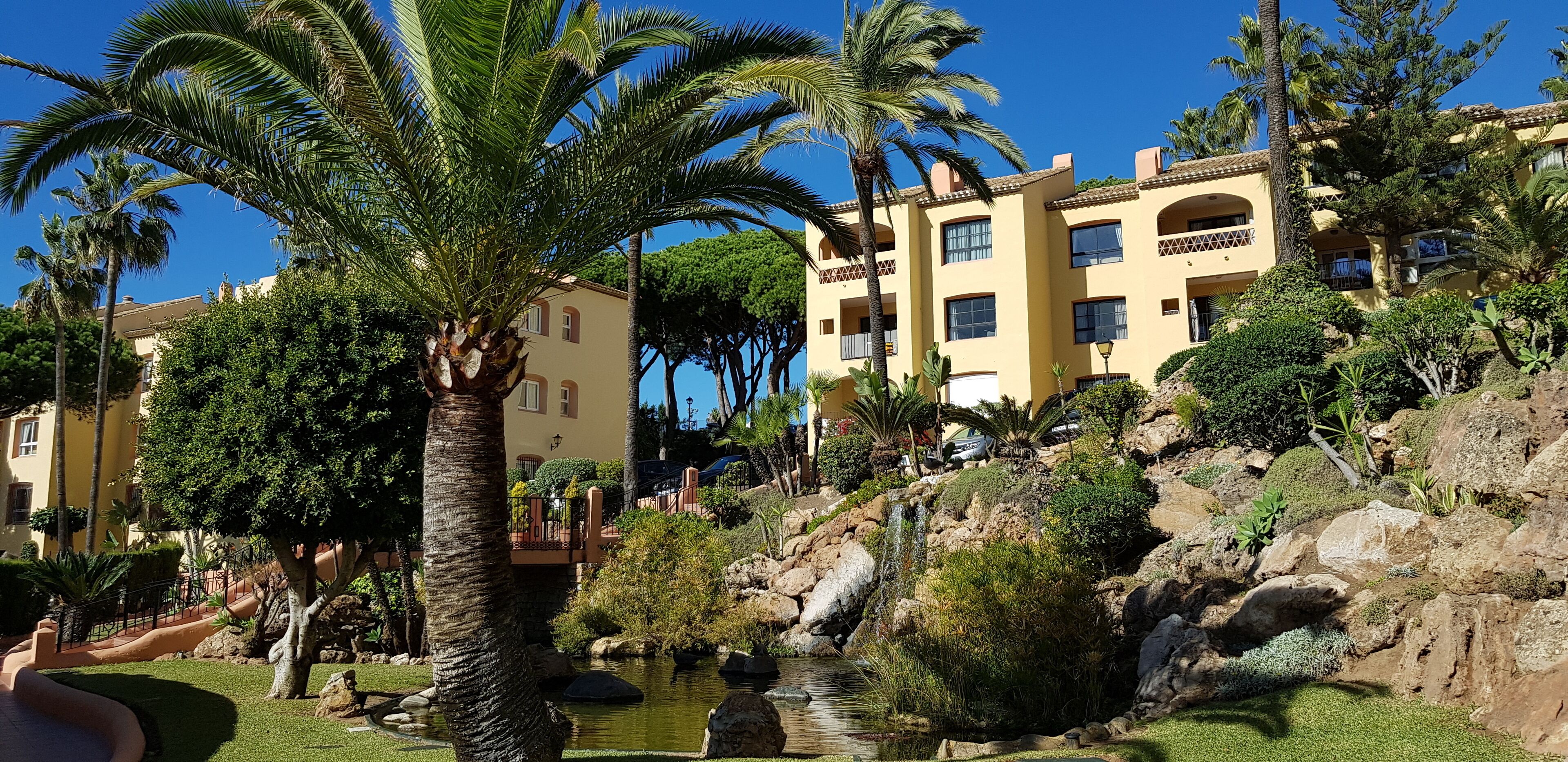 Un hotel con diversi balconi, una piccola cascata e un giardino con palme.