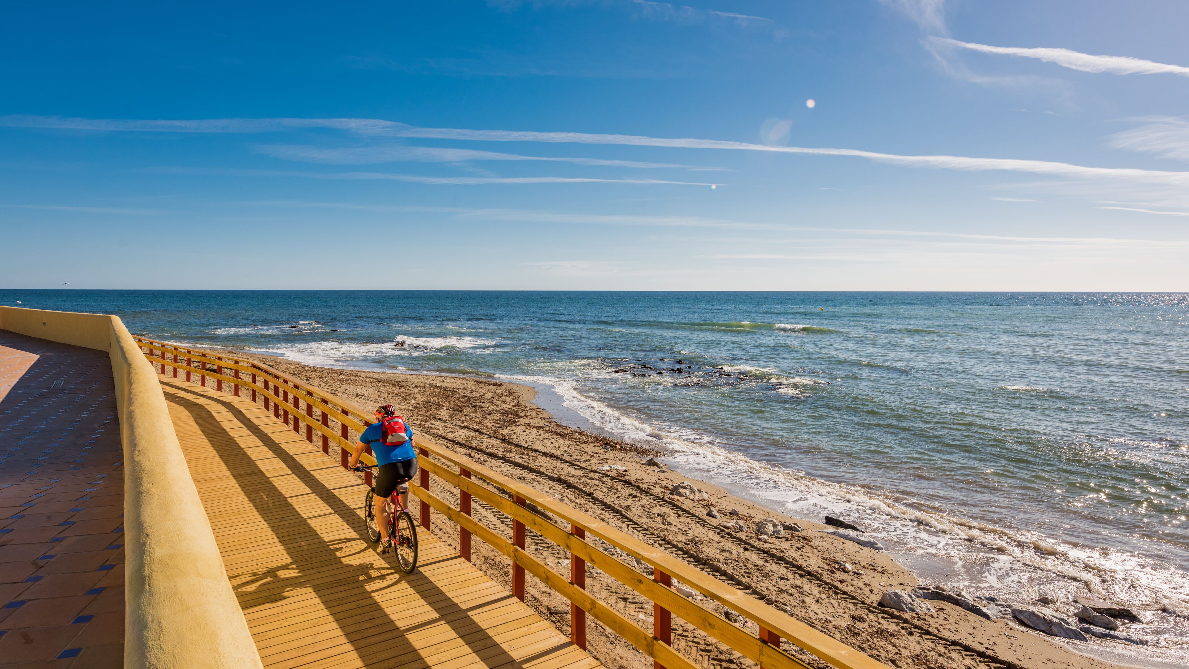 Un paseo marítimo de madera con barandilla amarilla, que conduce a una playa de arena y el océano al fondo.