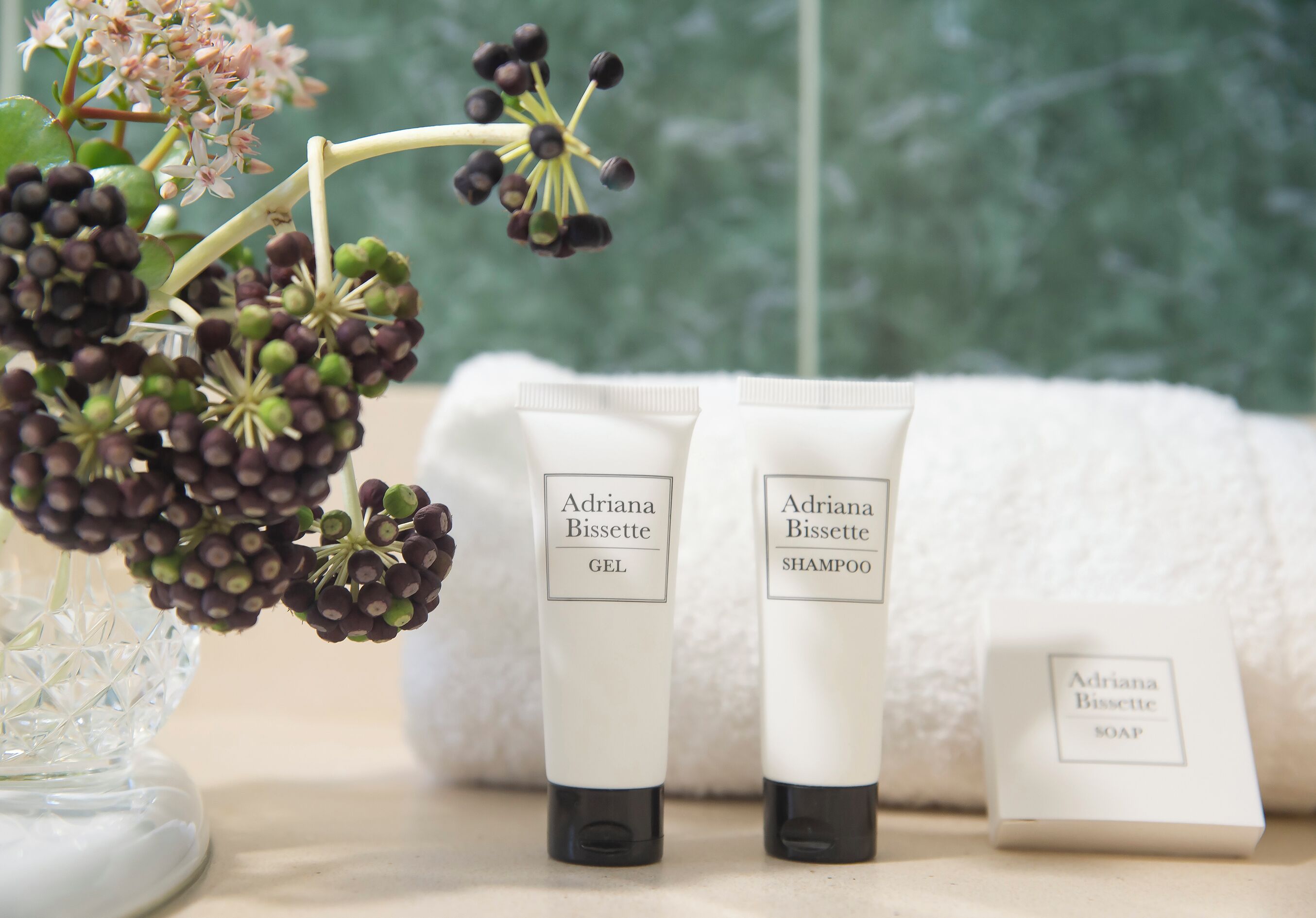 Un ensemble de produits de toilette comprenant du gel douche, du shampoing et du savon, disposés sur une table, avec un vase de fleurs en arrière-plan.