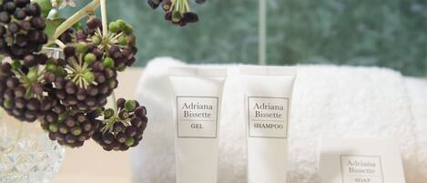 Un ensemble de produits de toilette comprenant du gel douche, du shampoing et du savon, disposés sur une table, avec un vase de fleurs en arrière-plan.